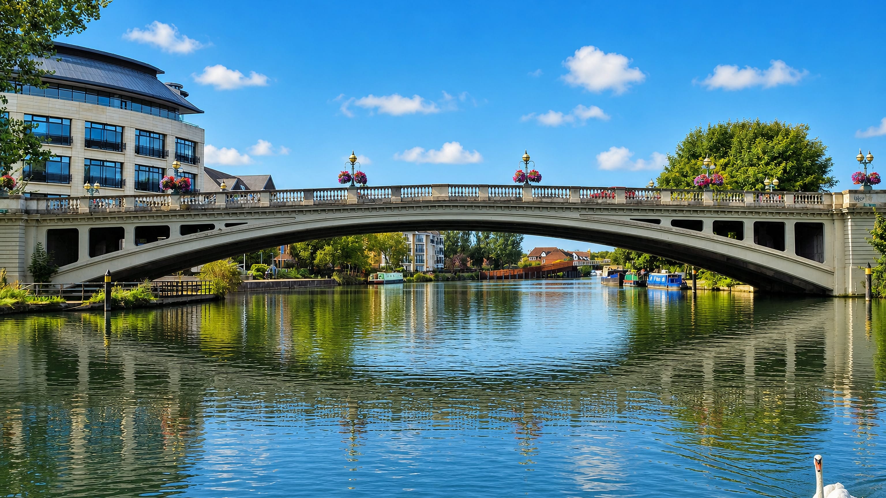 Reading Bridge arching over the Thames at Lower Caversham, with flower baskets, narrowboats and a swan.