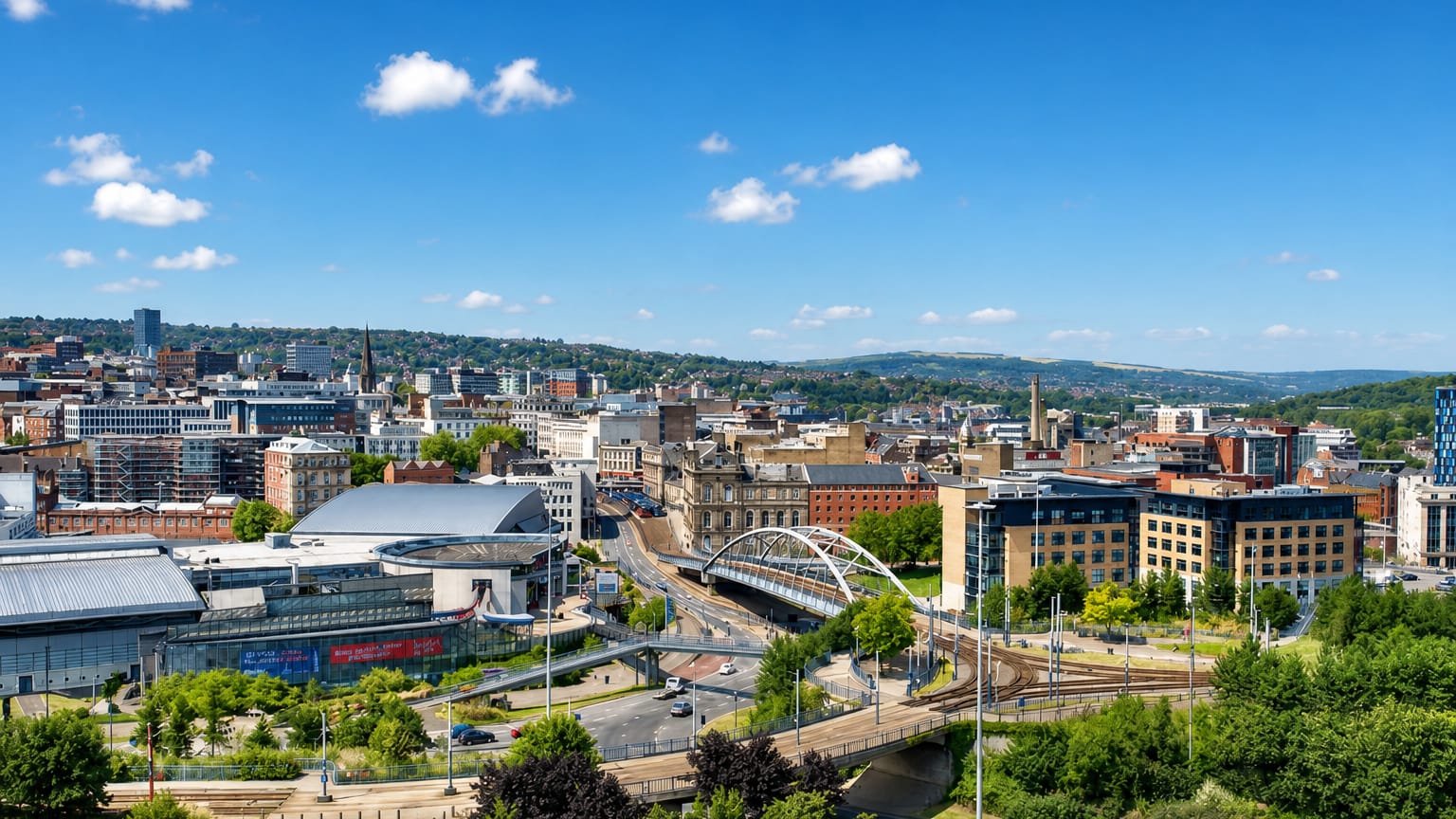 Sheffield city centre in daylight with the arched Park Square tram bridge, tram lines and green hills behind.