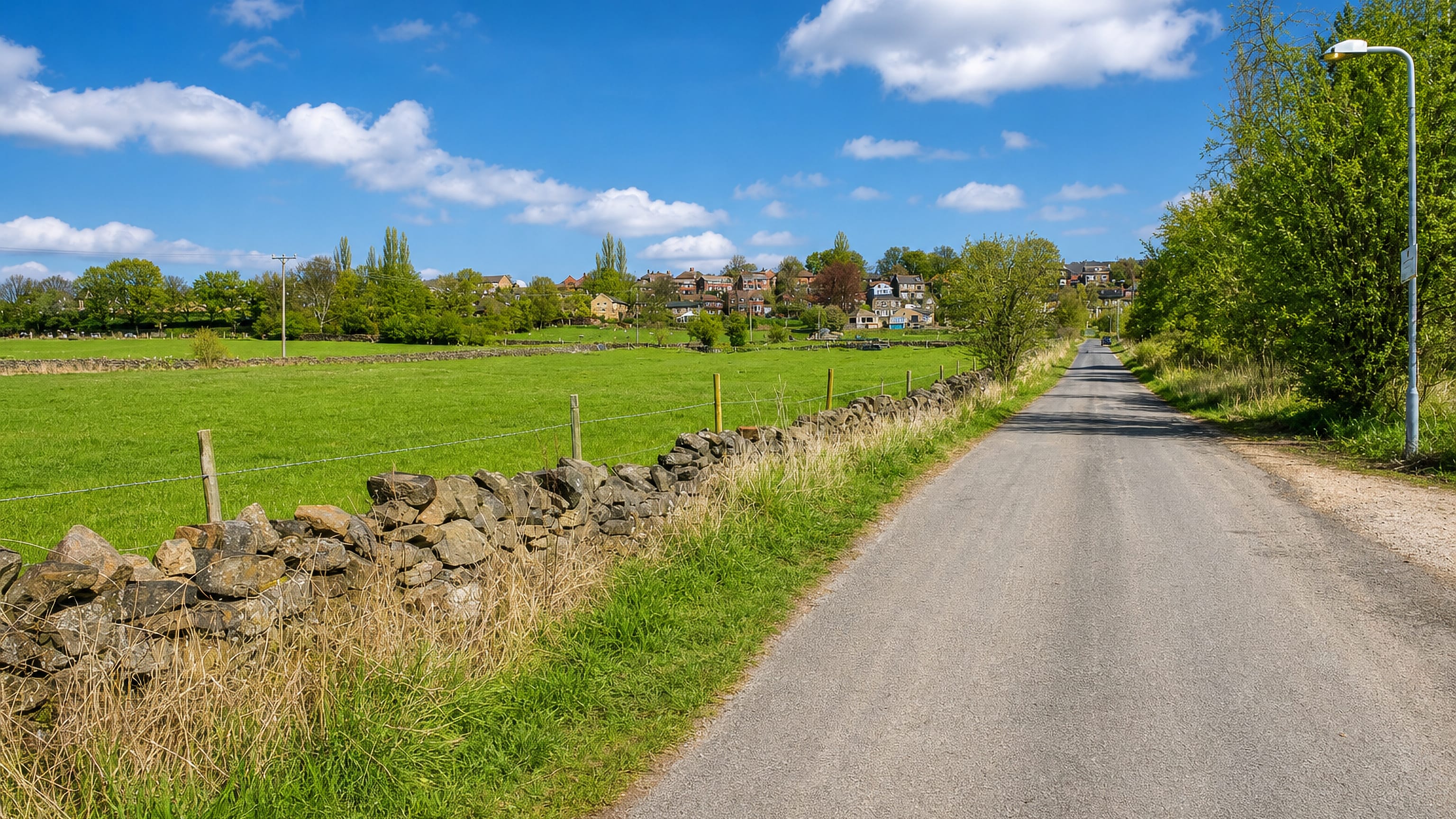 Country lane and drystone wall running past fields toward hillside houses at Wisewood, Sheffield, England.