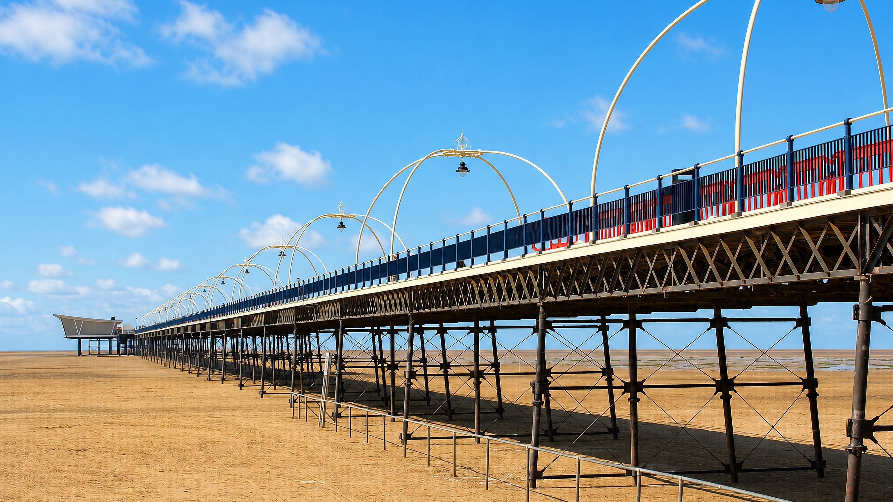 Southport Pier in England striding over the town's wide sand flats beneath a clear blue sky.