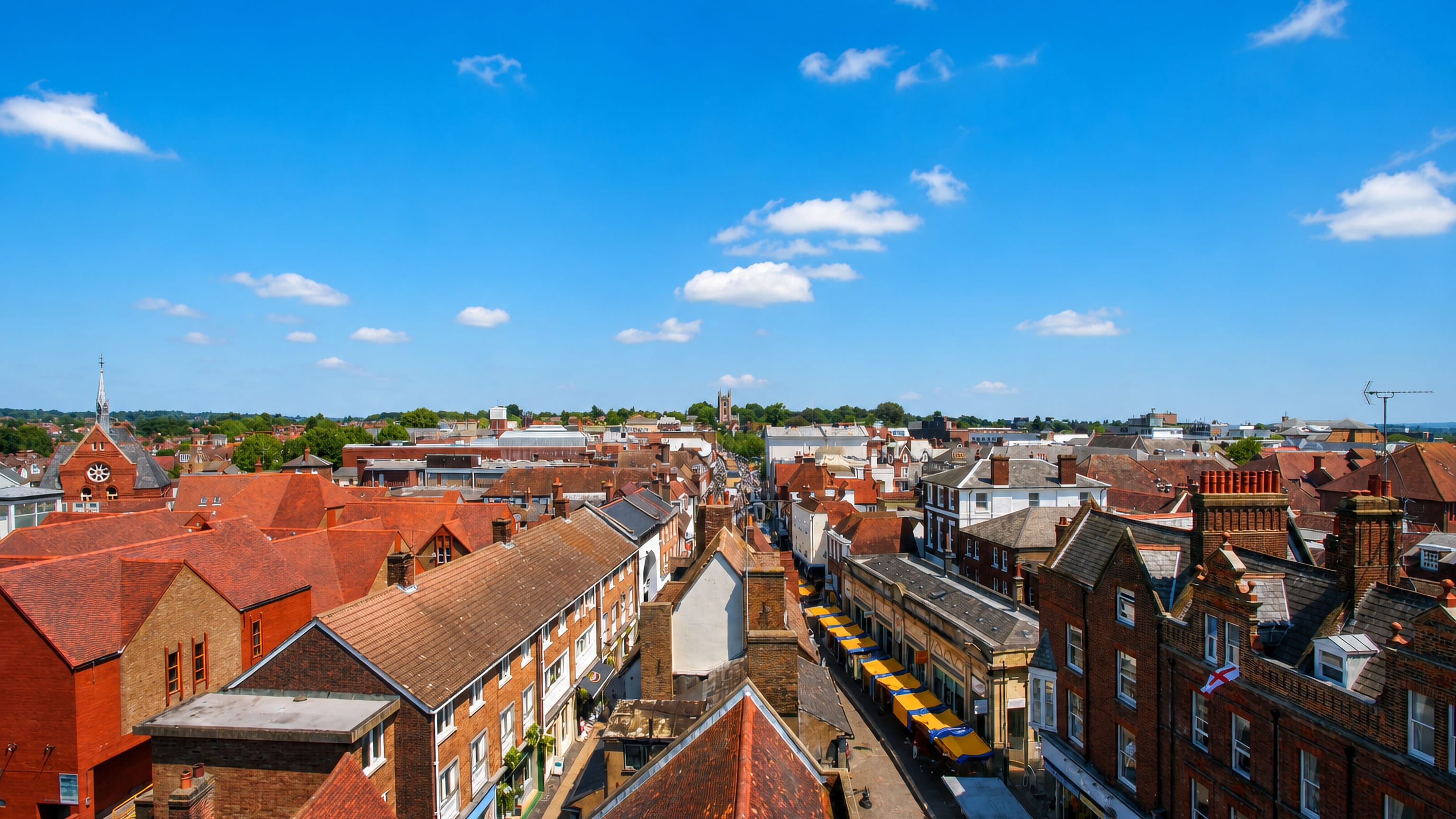 Red-tiled rooftops and a shop-lined high street under blue sky in St Albans, England