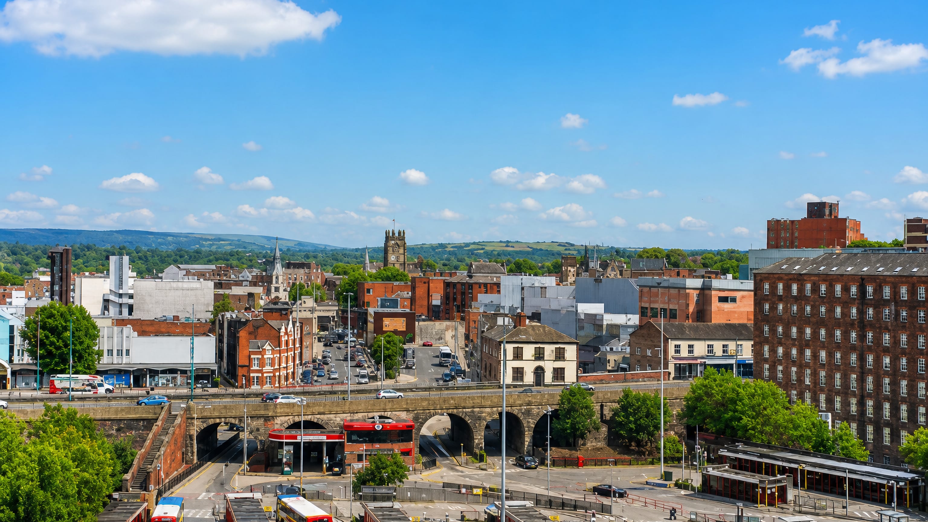 Stockport town centre from above: red-brick mill, arched road viaduct and bus station below the Pennine foothills.