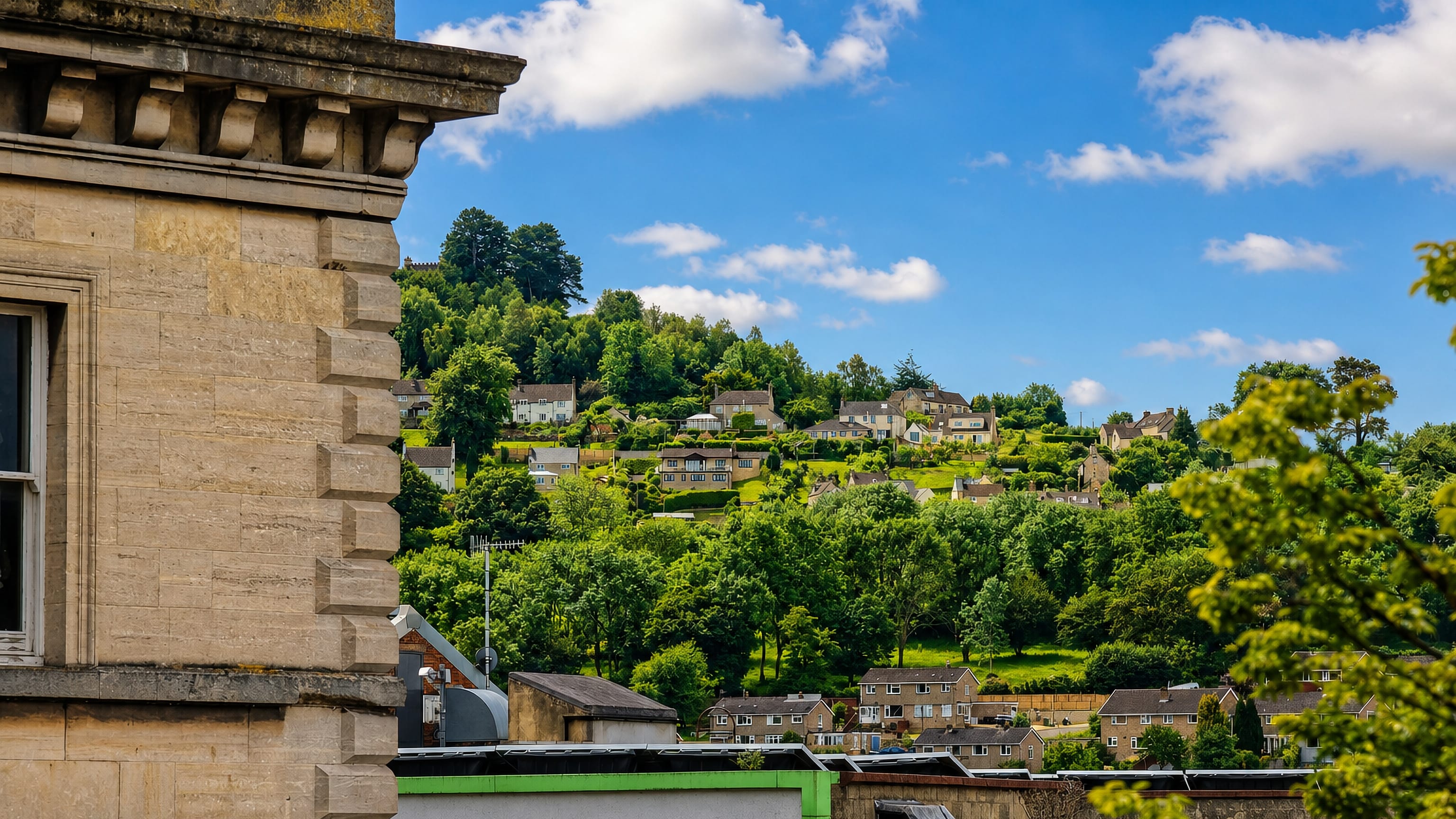 Cotswold-stone houses climbing the wooded valley slope above Stroud's rooftops in Gloucestershire.