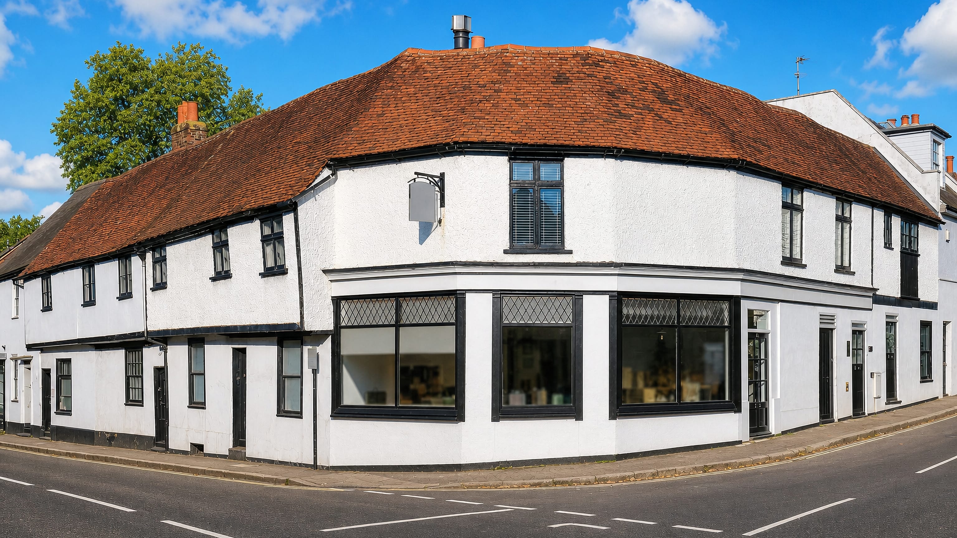 White-rendered tile-roofed corner shop building on a quiet street corner in Ewell, Surrey.