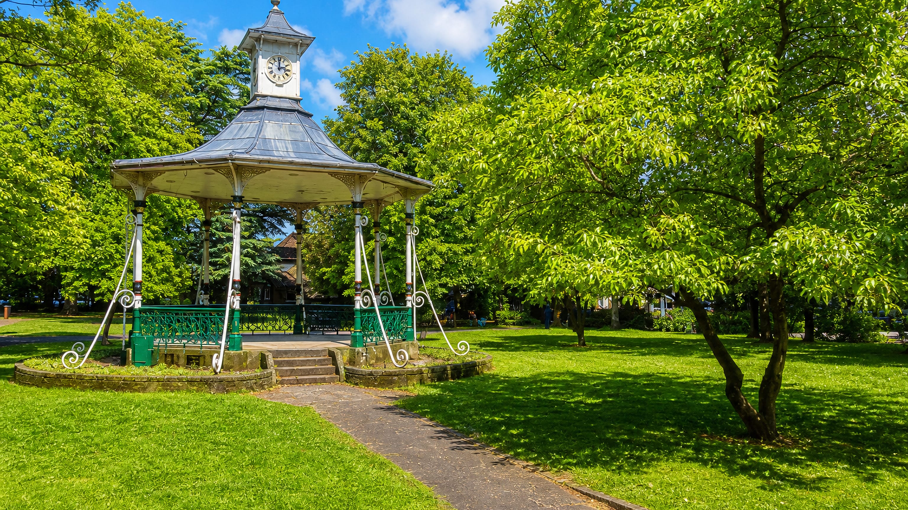 Ornate Victorian bandstand with a clock turret in a sunlit green park in Swindon, England.