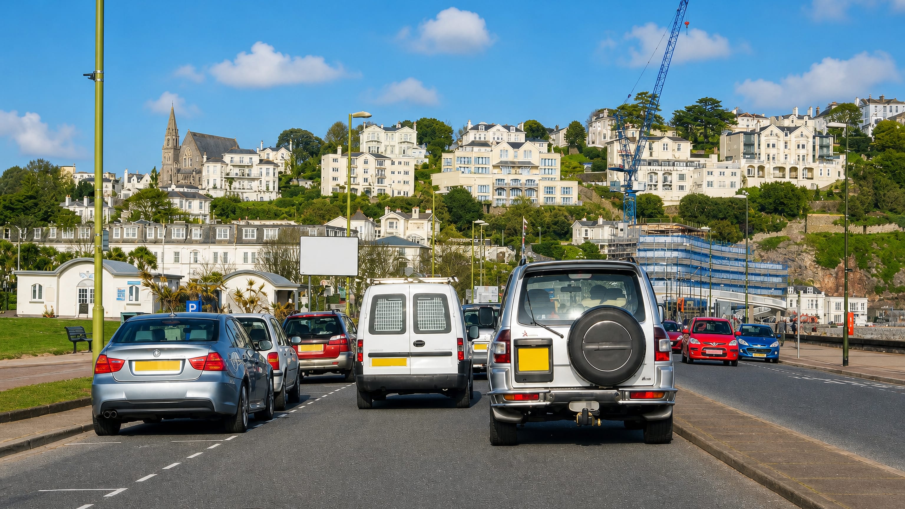Traffic on the seafront road below Chelston's white hillside villas and church spire in Torquay.
