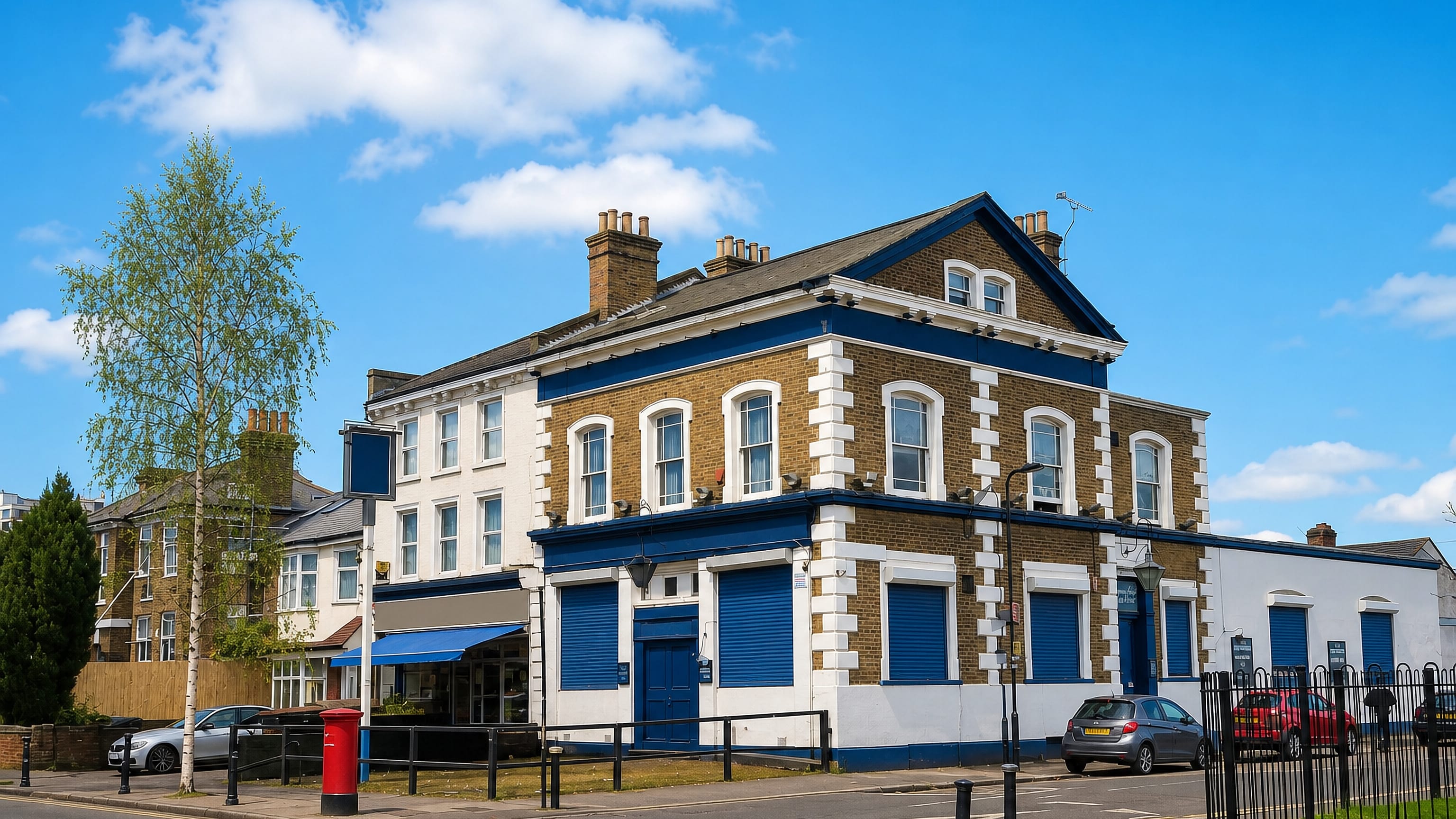 Yellow-brick corner pub and shuttered shopfronts with a red pillar box in Northumberland Park, Tottenham