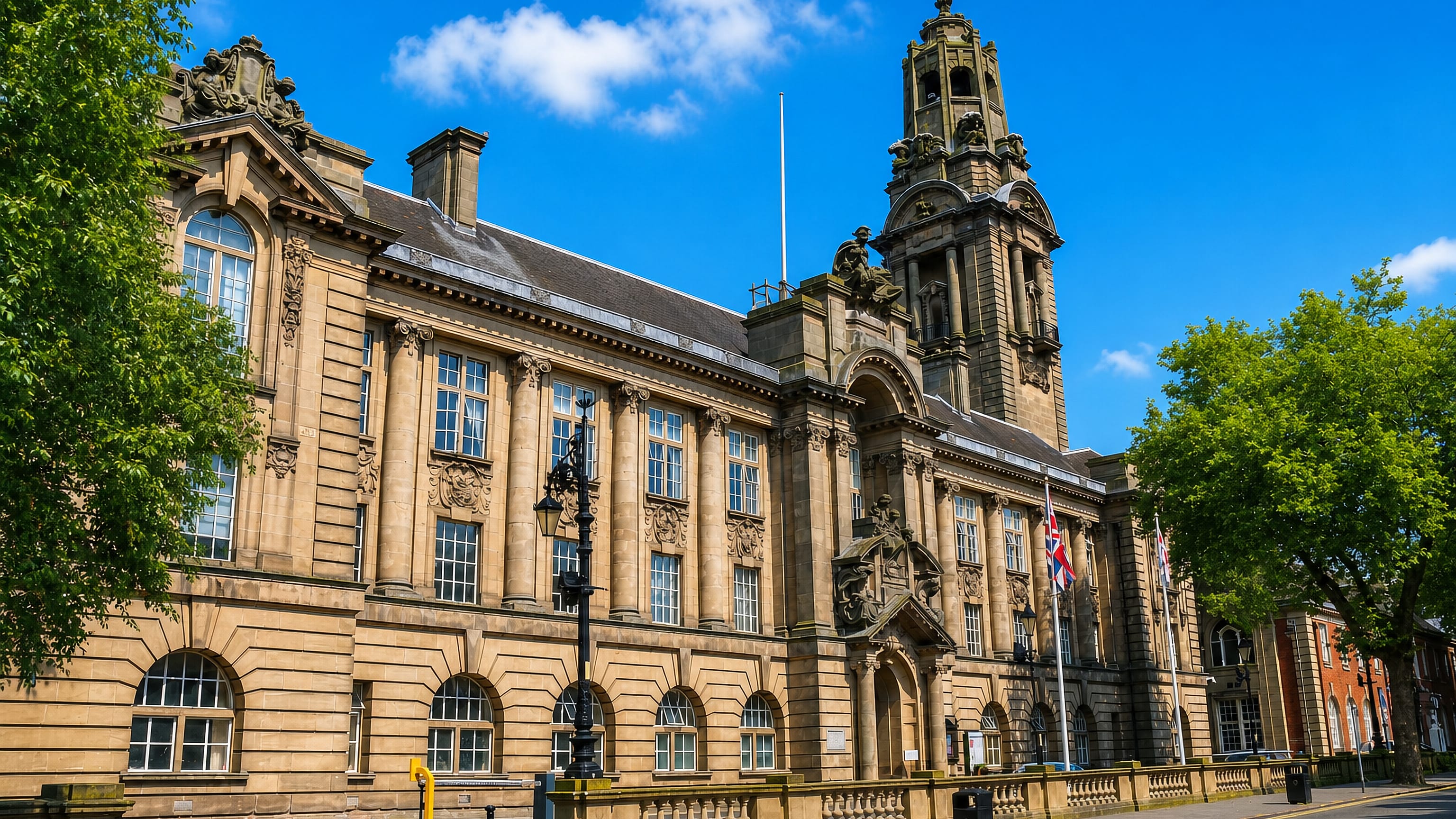 Walsall's sandstone civic hall and clock tower rising over a sunlit street lined with summer trees.