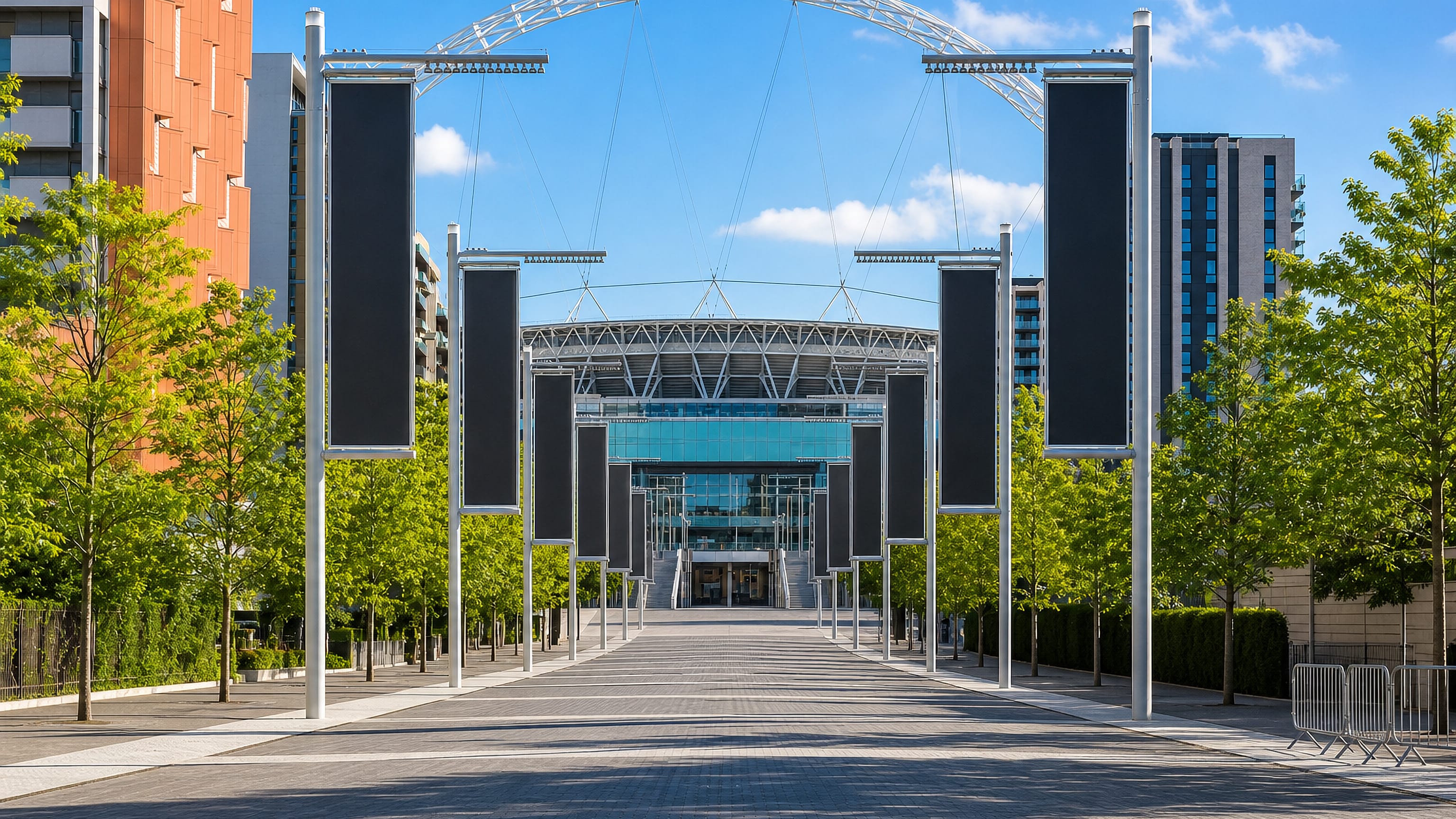 Olympic Way in Wembley Park, London, leading to Wembley Stadium and its steel arch under a blue sky.