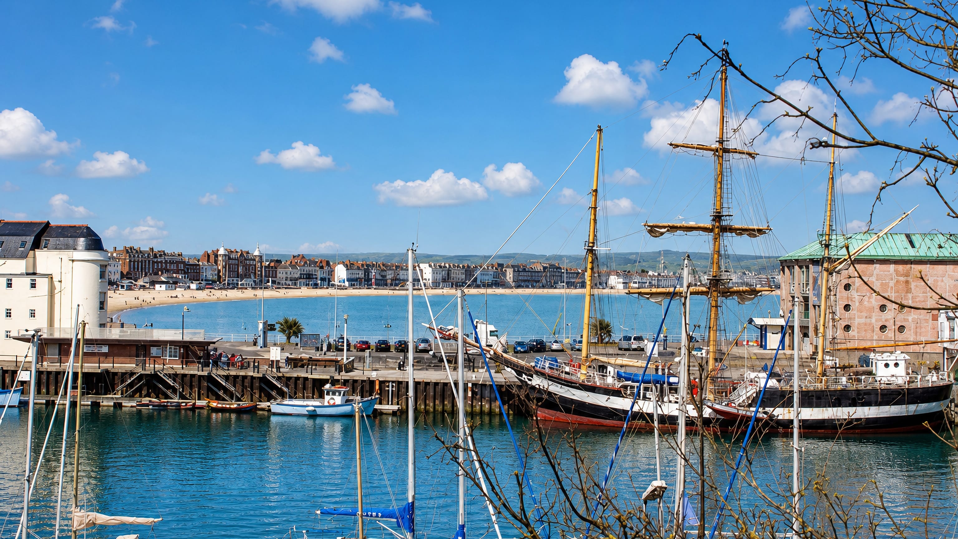 Weymouth harbour in Dorset, with tall-ship masts, moored yachts and the Georgian esplanade curving around the beach
