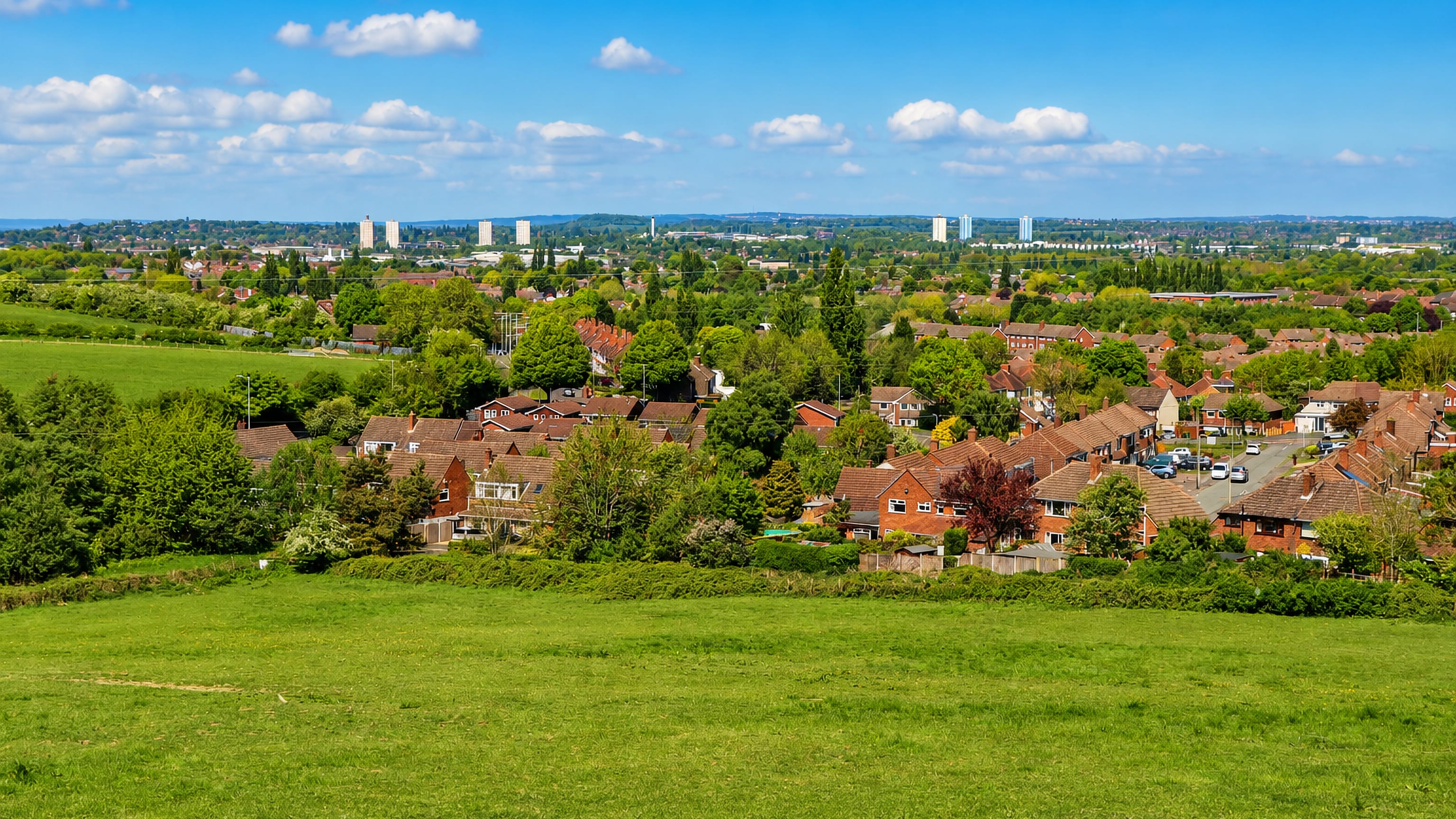 Grassy open ground overlooking red-brick housing in Ettingshall with Wolverhampton's tower blocks beyond.