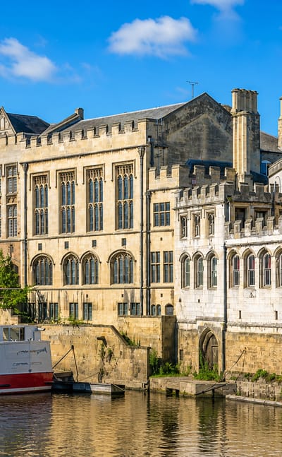 Medieval Gothic riverside buildings and the Guildhall lining the River Ouse in York, with a moored cruise boat.