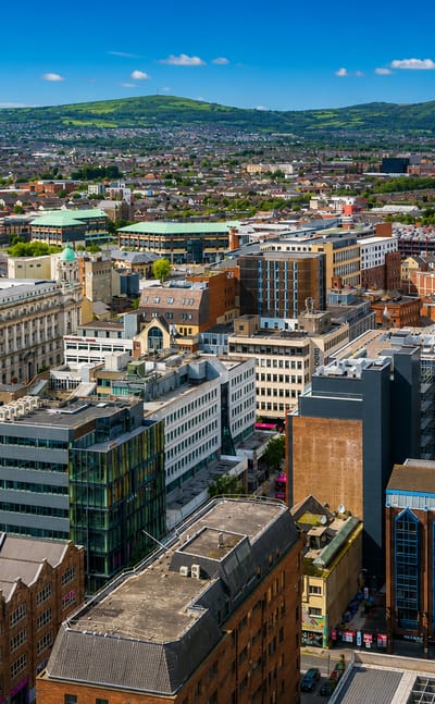 Aerial view over Belfast city centre with the domed City Hall and green hills rising behind