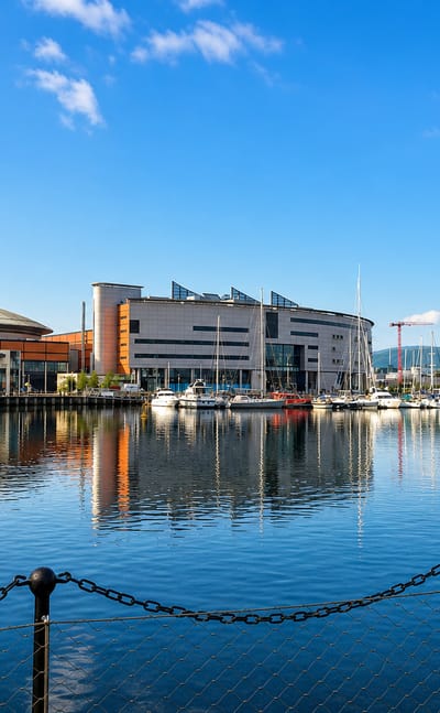 Belfast's Titanic Quarter waterfront with modern buildings, a marina and construction cranes reflected in the dock