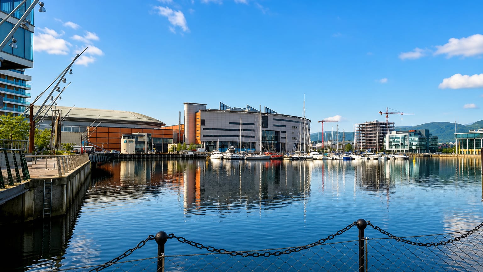 Belfast's Titanic Quarter waterfront with modern buildings, a marina and construction cranes reflected in the dock