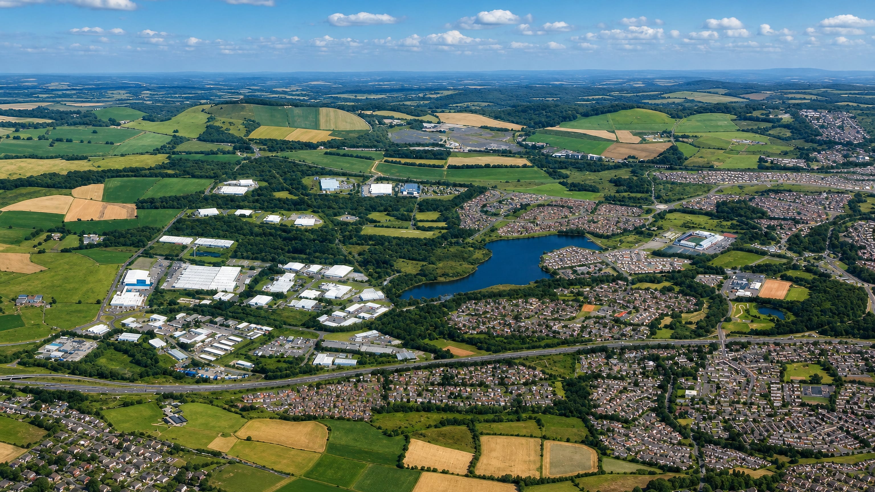 High aerial of Condorrat, Cumbernauld, with housing estates, a loch and business parks amid farmland.