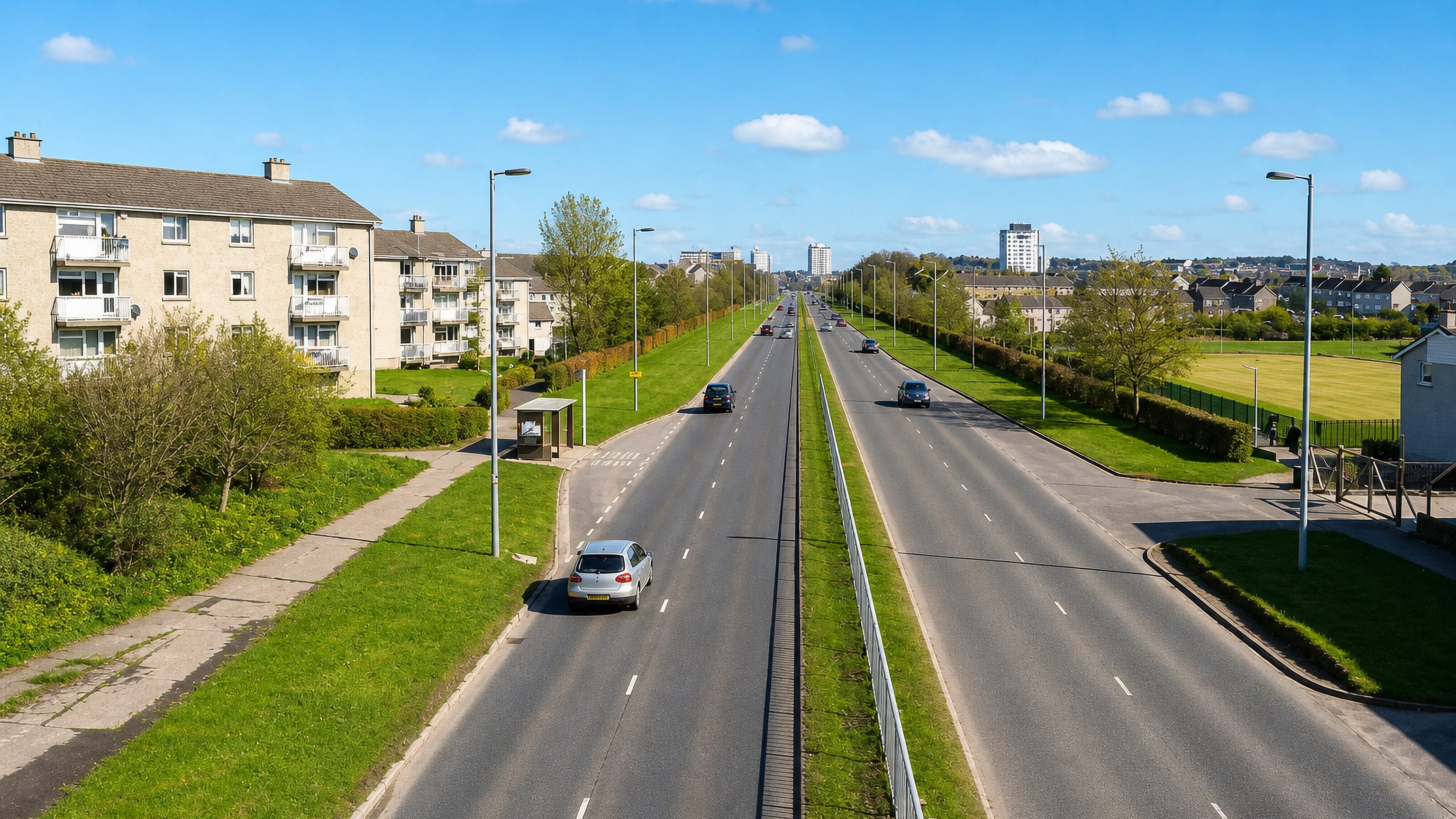 Dual carriageway, grass verges and low-rise flats with distant tower blocks in East Kilbride, Scotland.