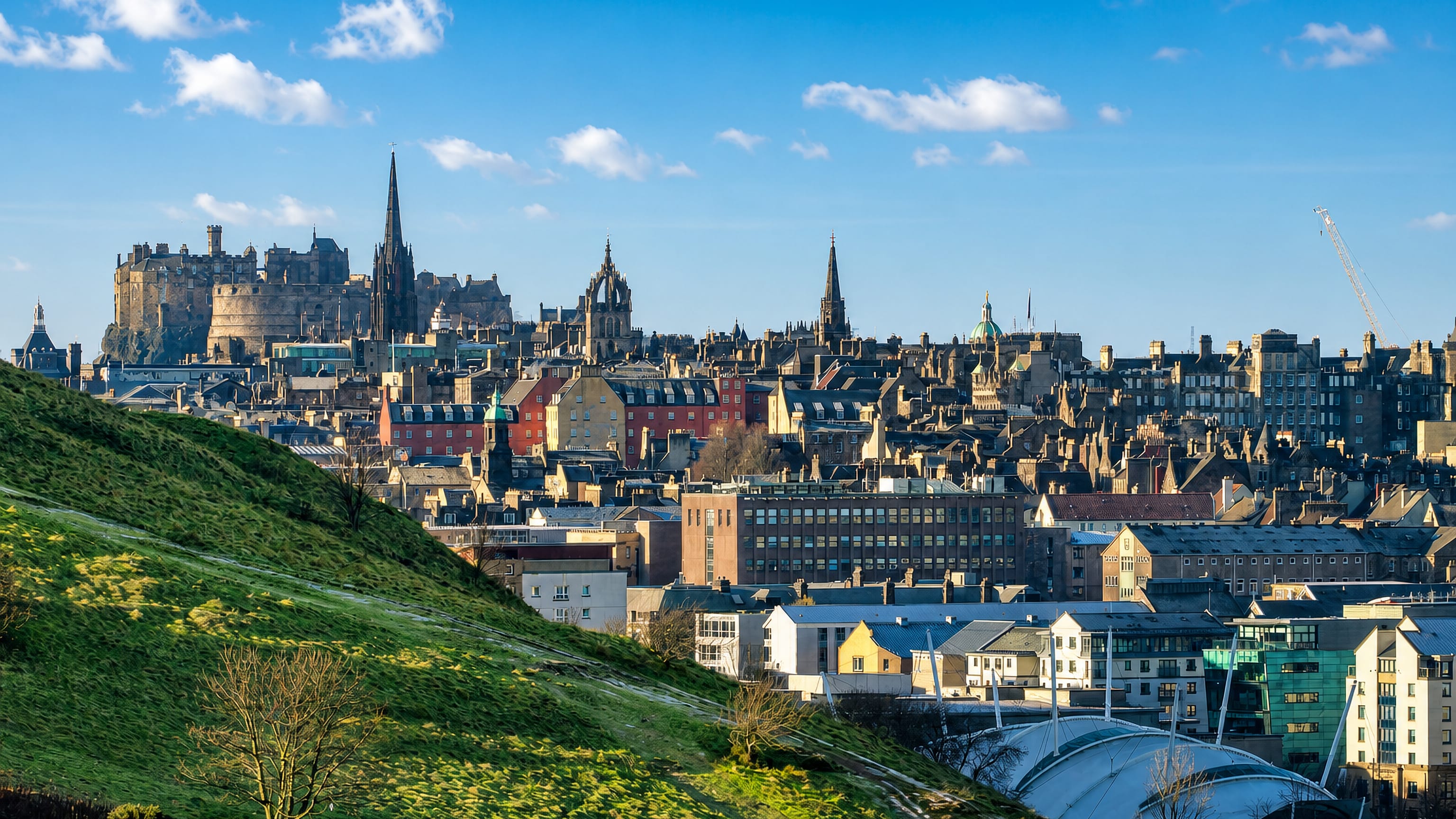Edinburgh Castle and Old Town spires rising above the city, seen from the grassy slopes of Holyrood Park