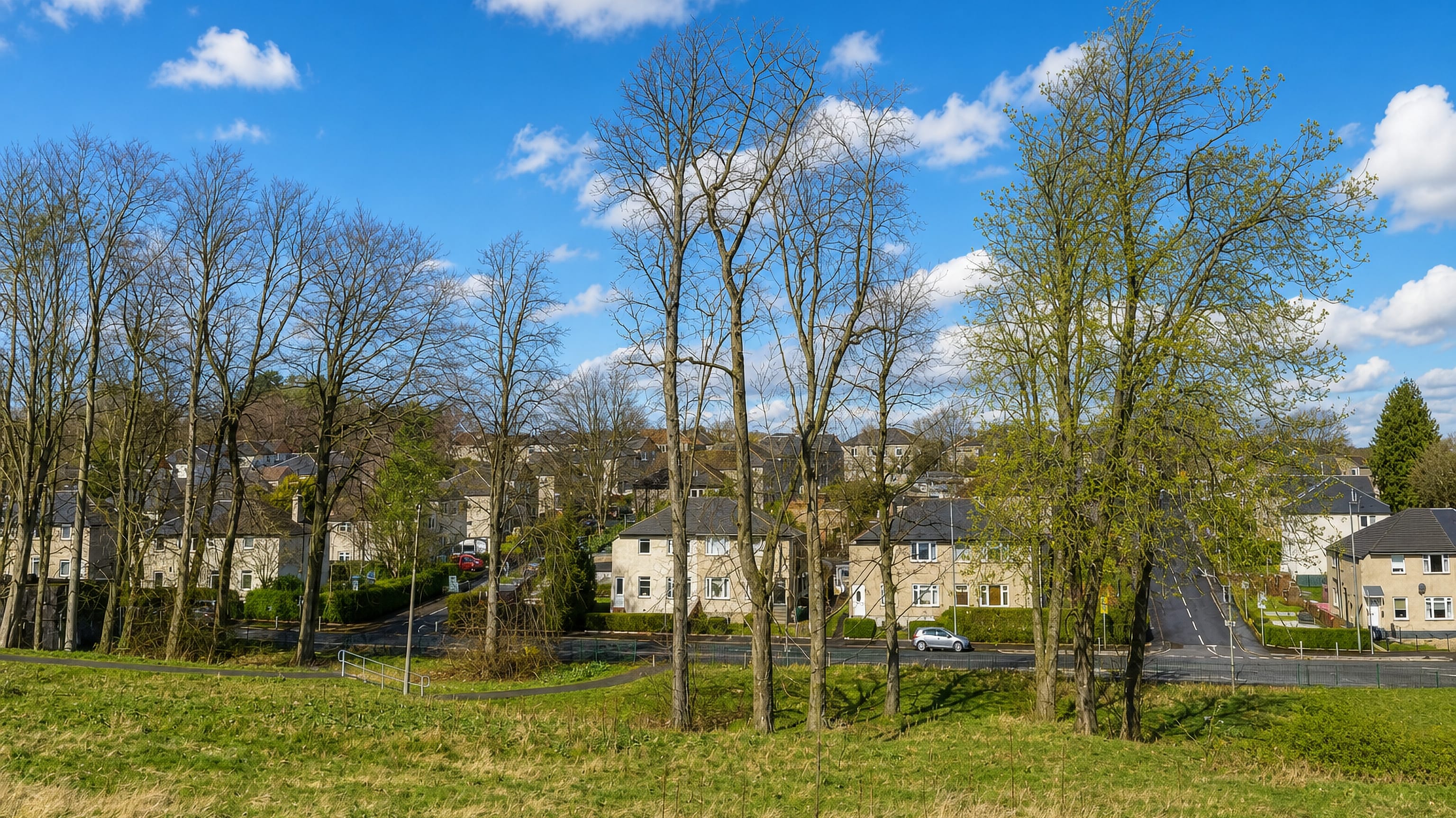 Stone-fronted semi-detached homes and open grassland in Croftfoot, a residential suburb of southern Glasgow.