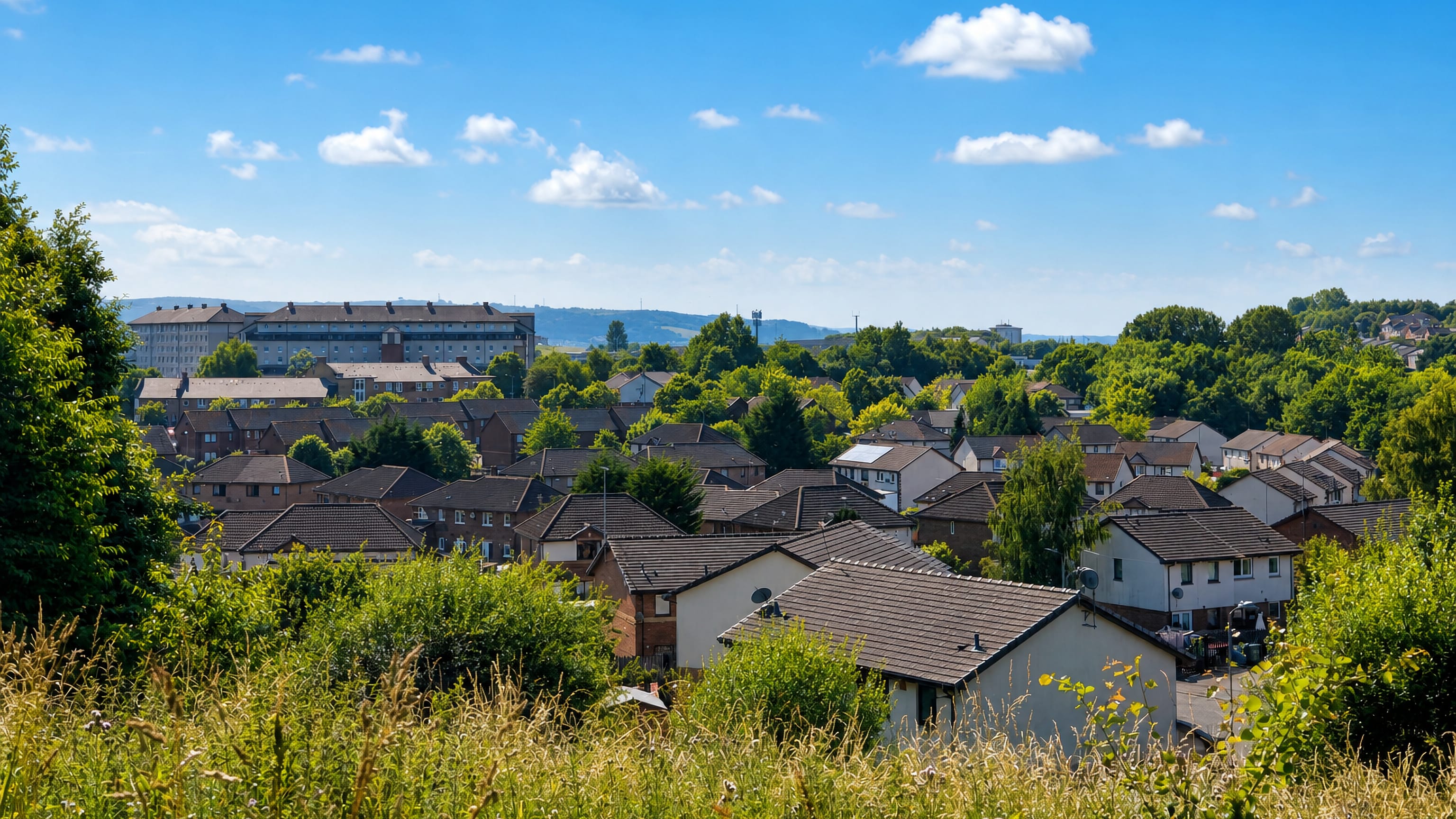 Rooftops of Darnley's housing estates in southern Glasgow, framed by trees and distant hills.