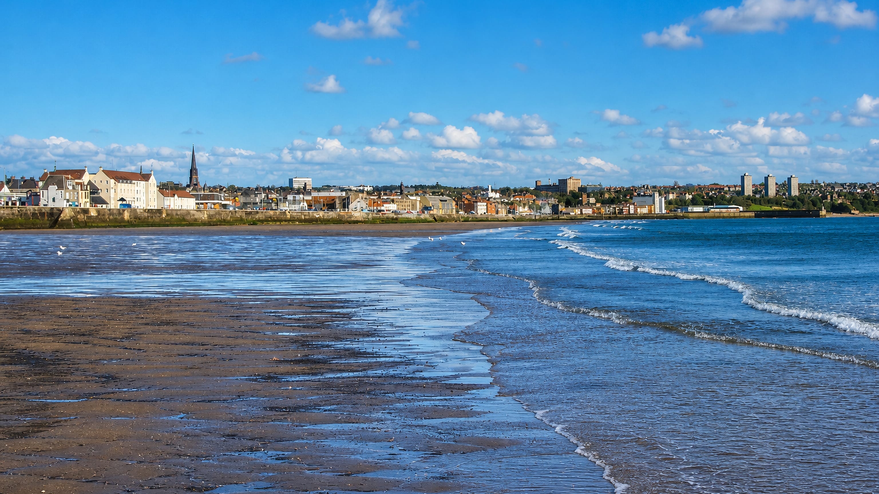 Kirkcaldy's seafront and church spire across the wide sands of the Firth of Forth at low tide.