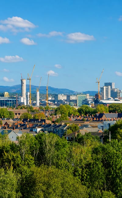 Cardiff skyline with the Principality Stadium arch, Wales Millennium Centre, and city towers rising beyond leafy terraced rooftops.