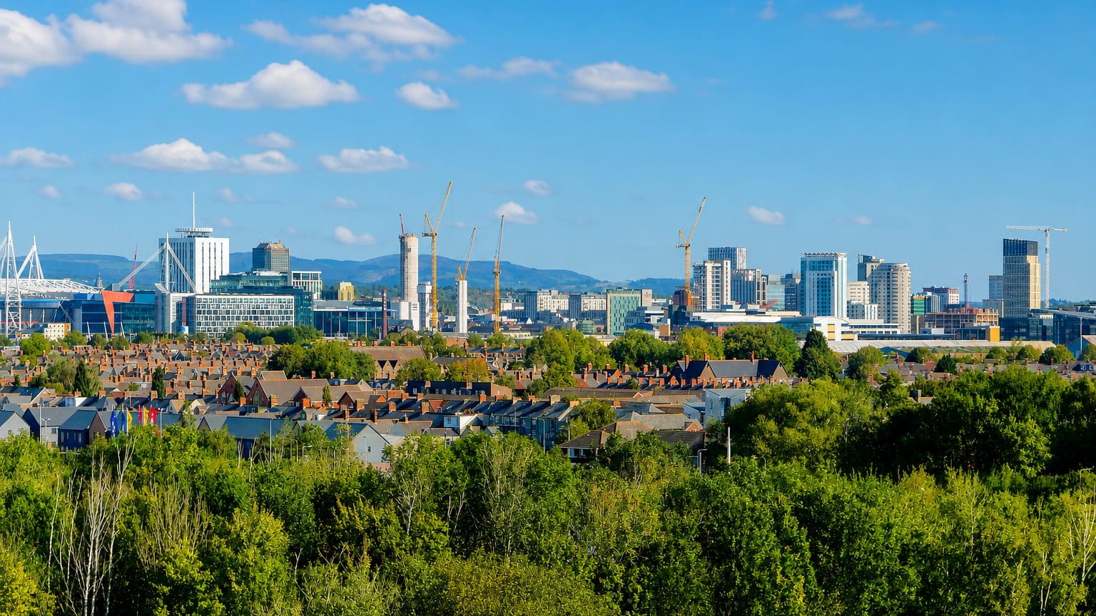 Cardiff skyline with the Principality Stadium arch, Wales Millennium Centre, and city towers rising beyond leafy terraced rooftops.