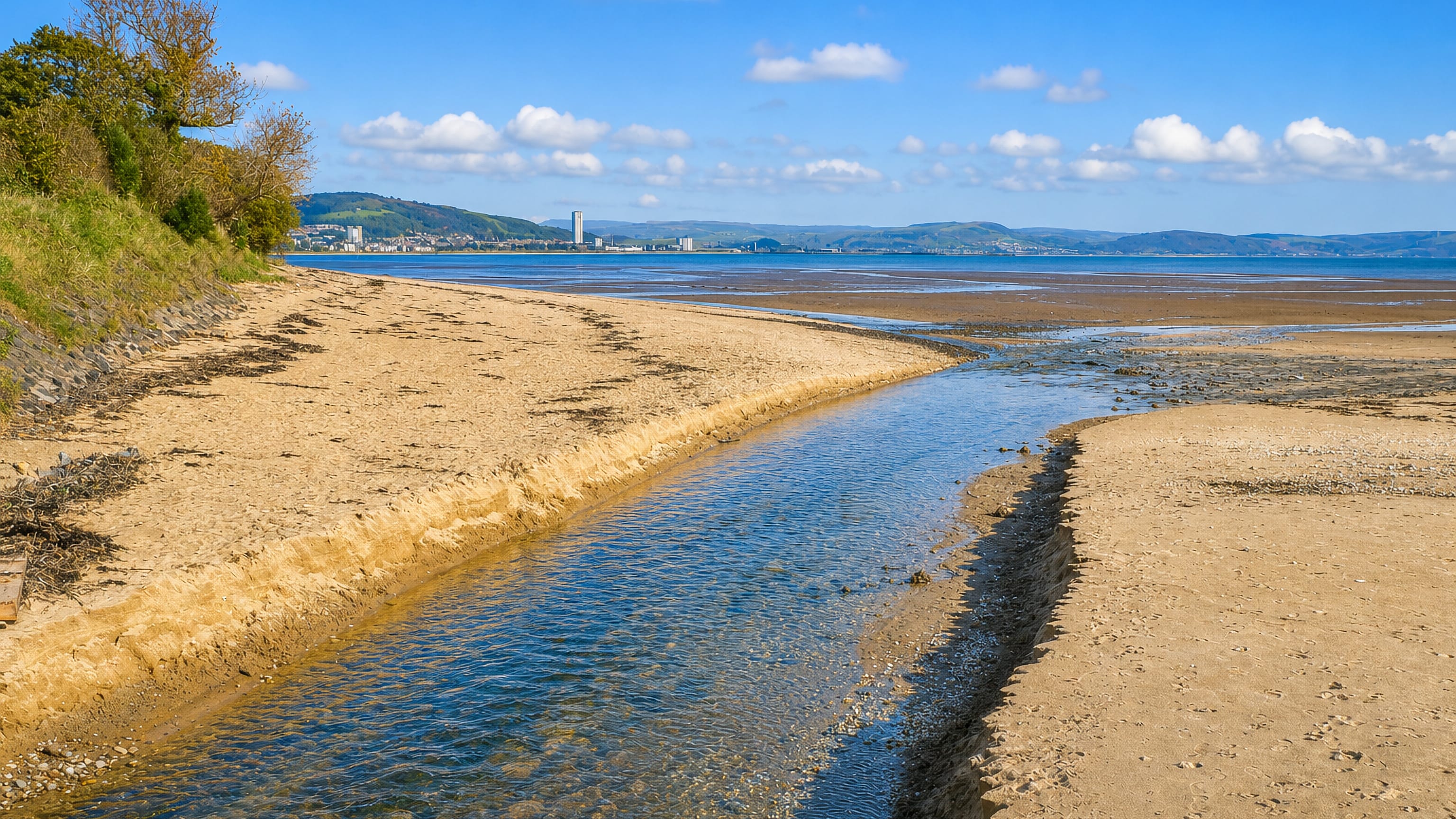 The Clyne stream crossing Blackpill beach at low tide, with Swansea's Meridian Tower beyond.