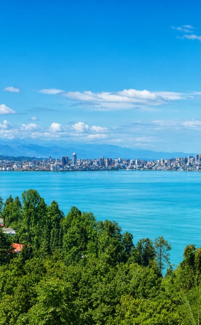 Batumi's high-rise skyline on the Black Sea coast with wooded hills and turquoise bay in the foreground