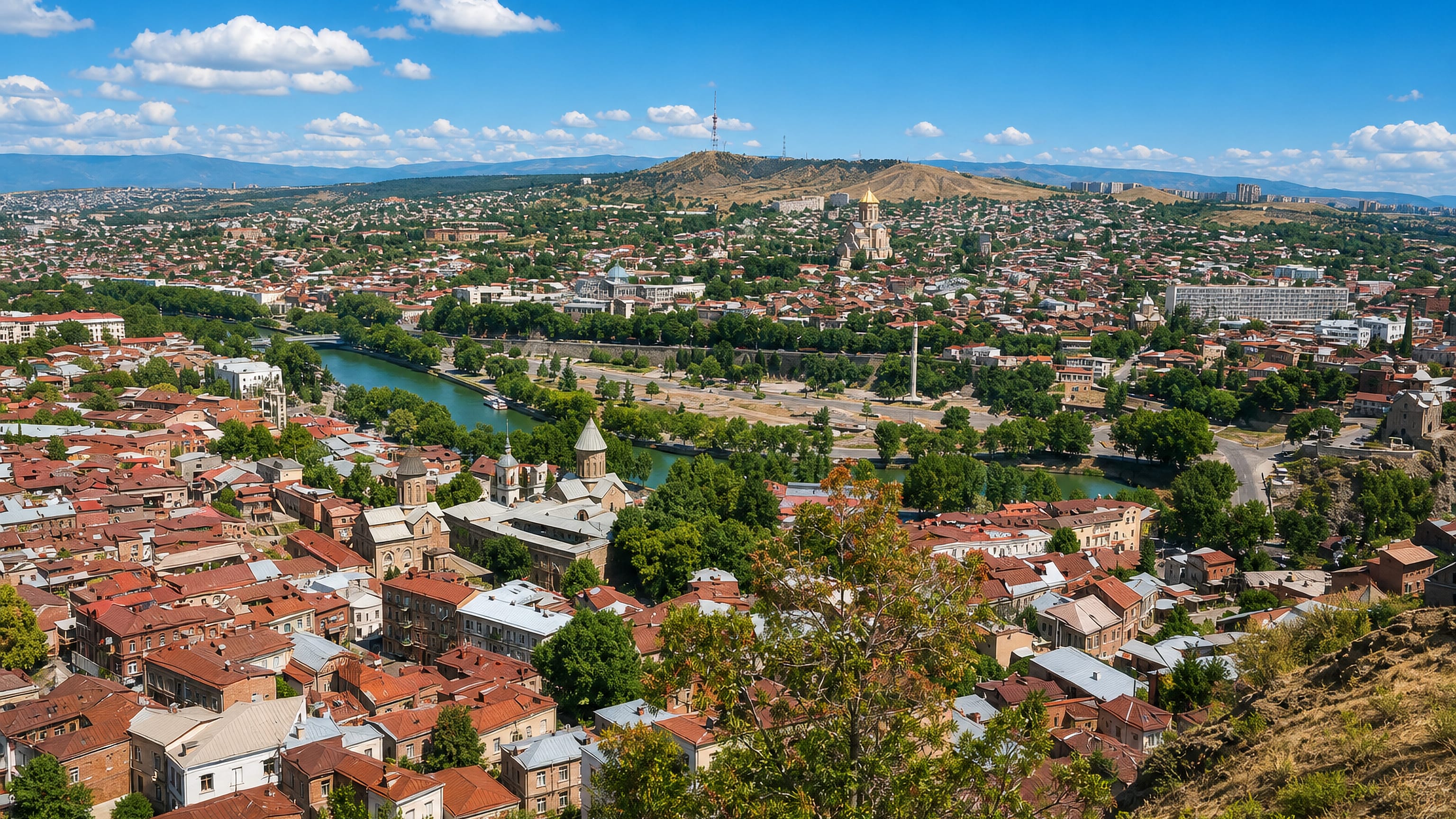 Panorama over Sololaki's tiled rooftops in Tbilisi toward the Mtkvari river and the golden-domed Holy Trinity Cathedral.