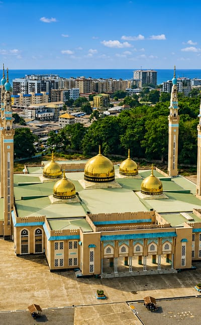 Conakry's Grand Mosque with golden domes and minarets before the city skyline and the Atlantic Ocean.