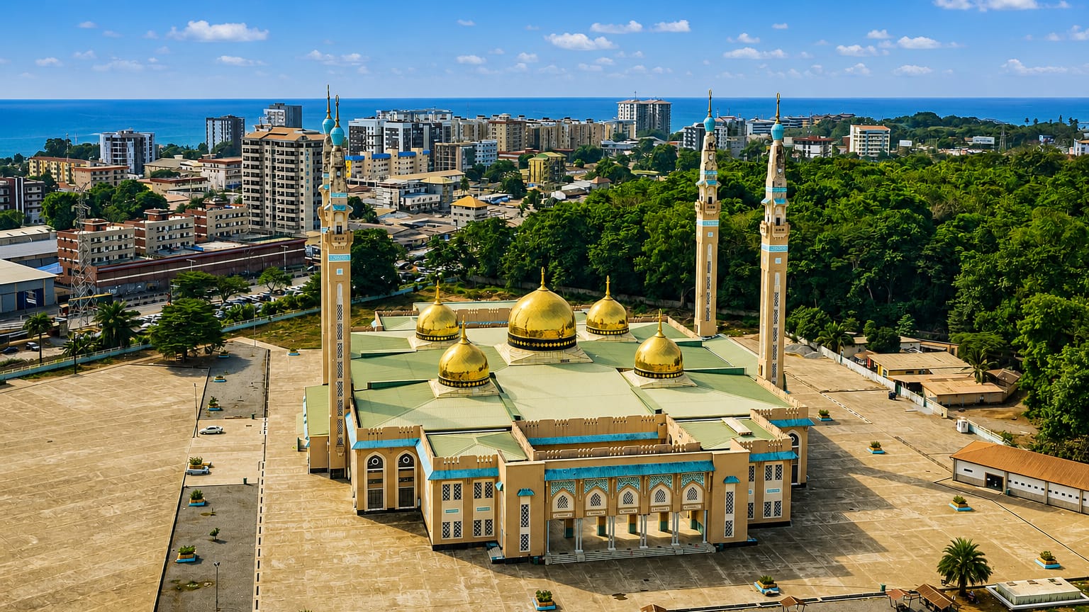 Conakry's Grand Mosque with golden domes and minarets before the city skyline and the Atlantic Ocean.