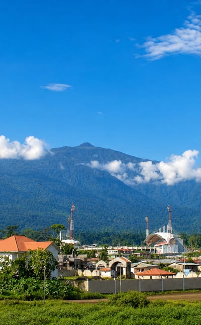 Malabo's low-rise buildings and a white modern mosque at the forested foot of the towering Pico Basile volcano