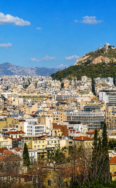 Athens cityscape of dense white buildings with Mount Lycabettus and mountains in the background, Greece.