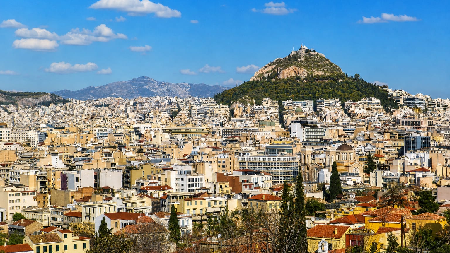 Athens cityscape of dense white buildings with Mount Lycabettus and mountains in the background, Greece.