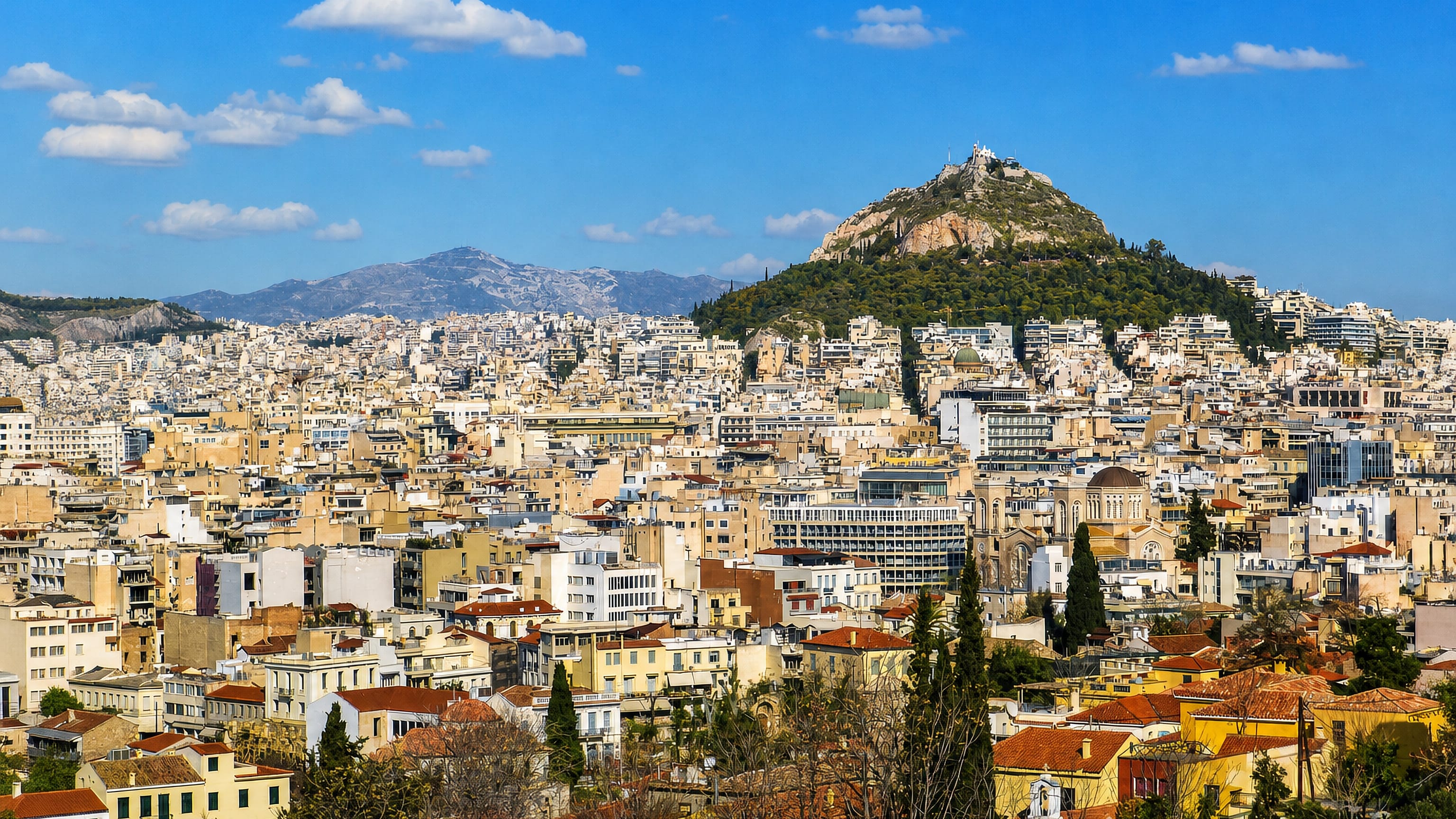 Athens cityscape of dense white buildings with Mount Lycabettus and mountains in the background, Greece.