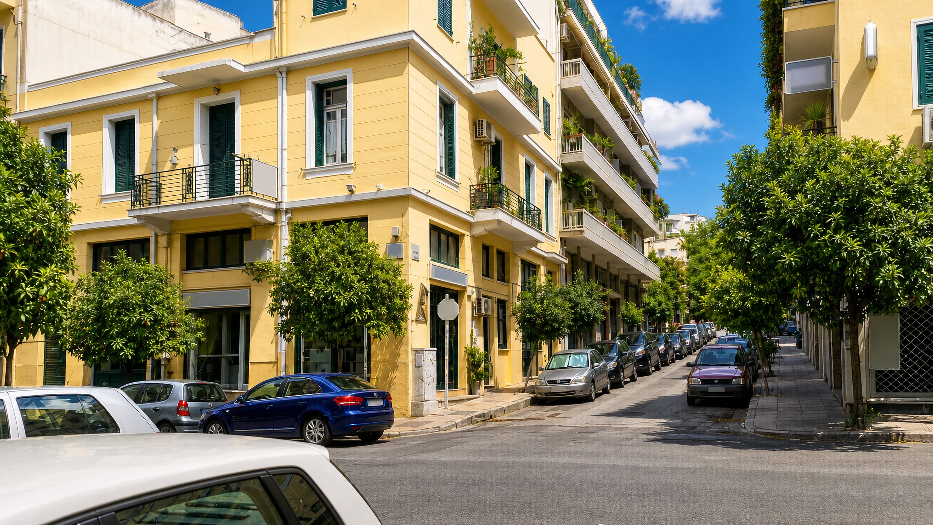 A quiet Koukaki street in Athens lined with yellow apartment buildings, balconies and orange trees.