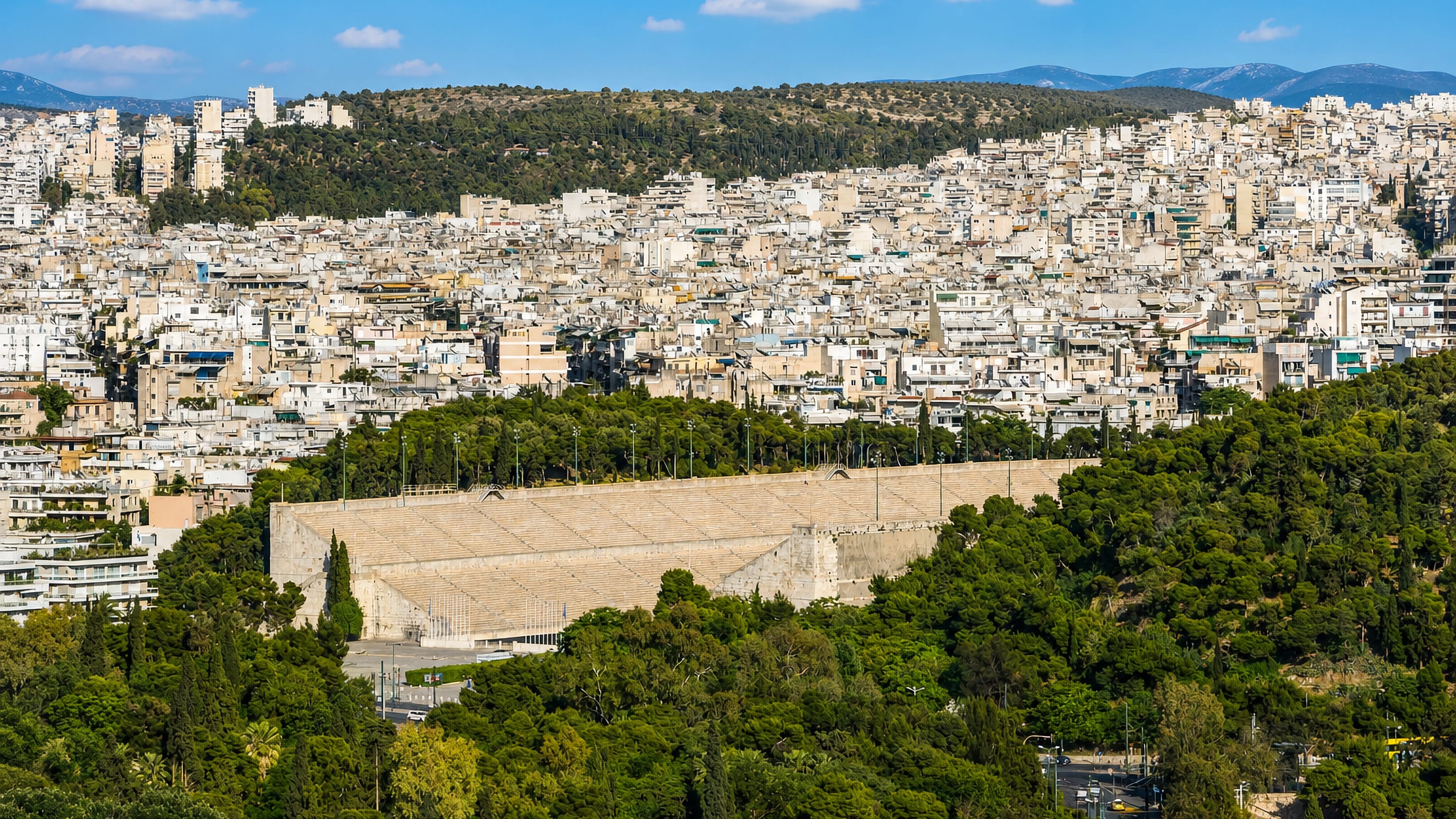 The marble Panathenaic Stadium ringed by pines below the dense rooftops of Pangrati, Athens.