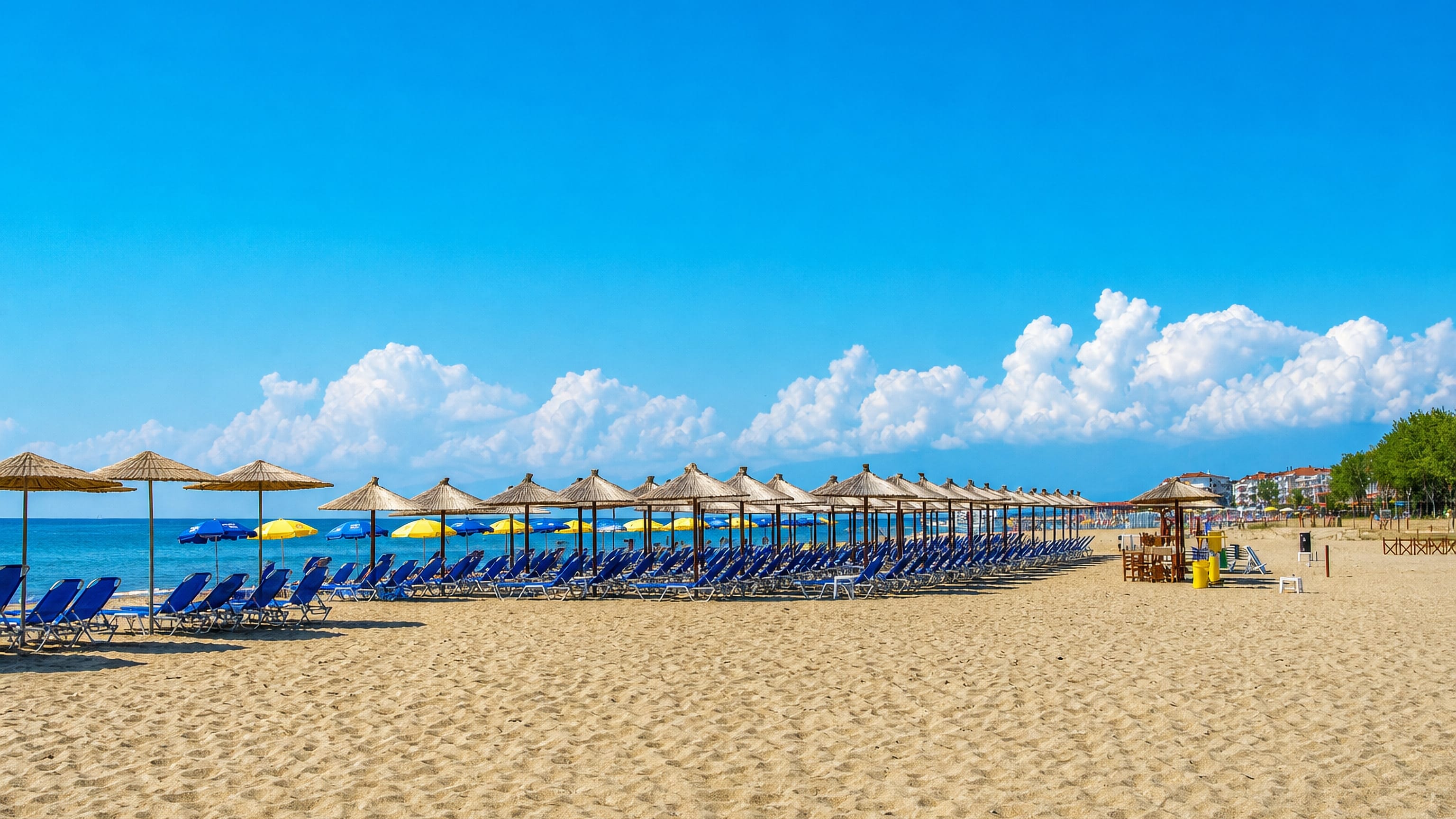 Rows of straw parasols and blue loungers on the sandy beach at Paralia, near Kateríni, Greece.