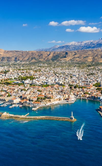 Chania's Venetian harbour and lighthouse below the snow-capped White Mountains on Crete.