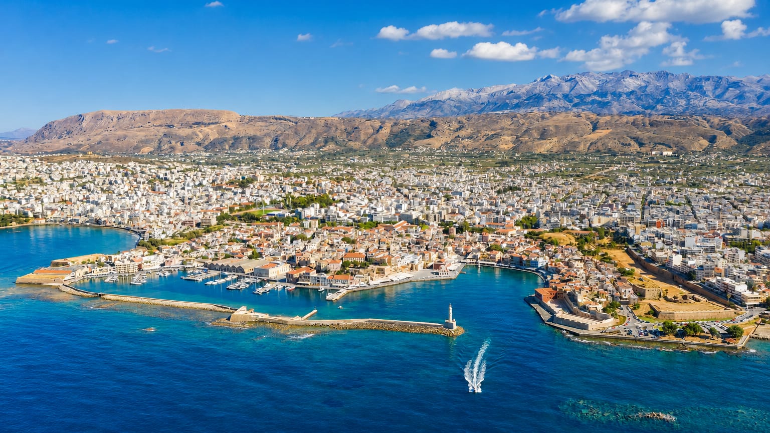 Chania's Venetian harbour and lighthouse below the snow-capped White Mountains on Crete.