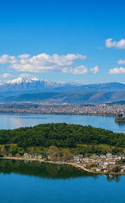 The wooded island on Lake Pamvotida with the city of Ioannina and snow-capped mountains beyond.