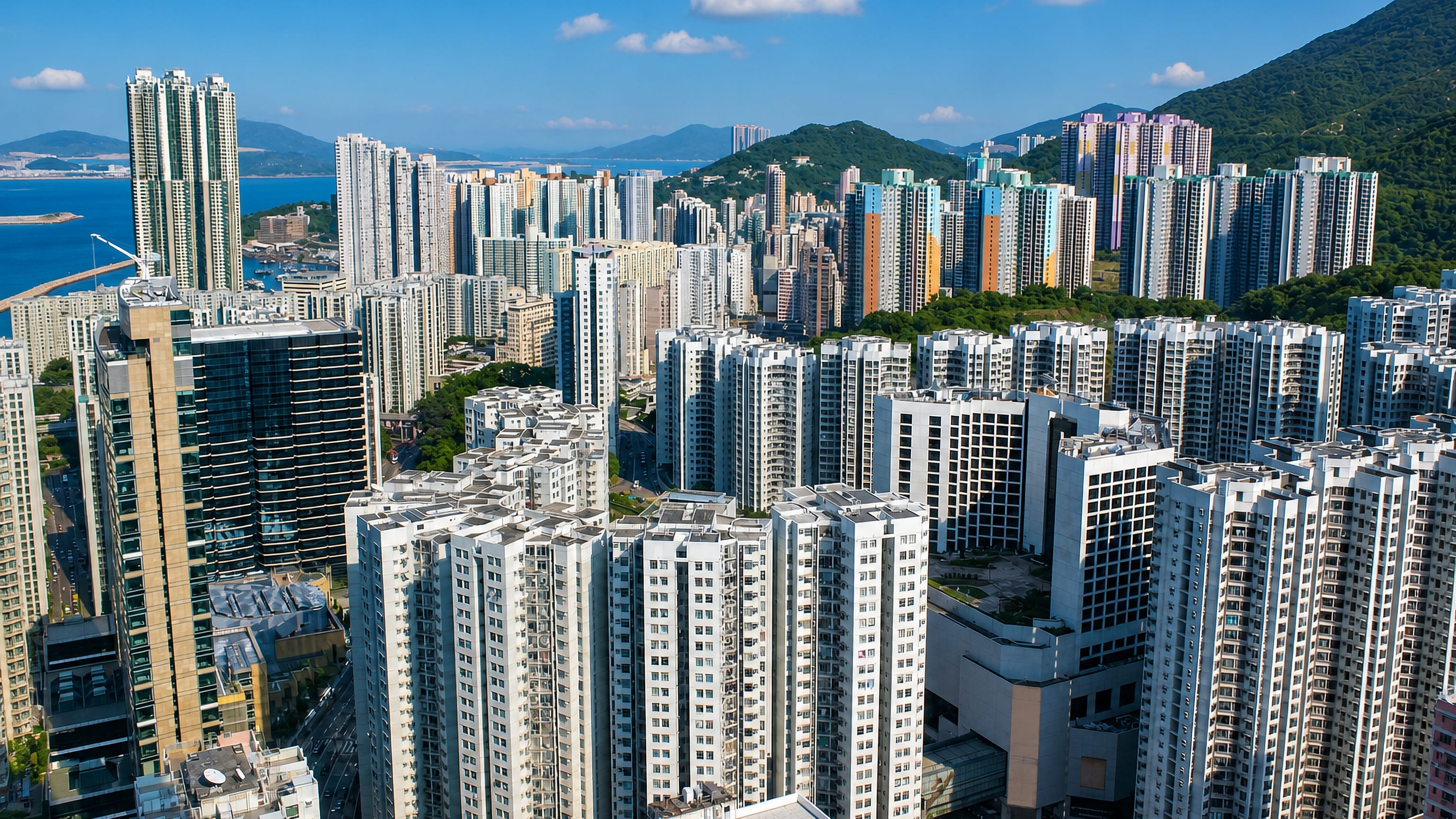 Dense residential high-rises rising between green hills and the sea on Hong Kong Island.
