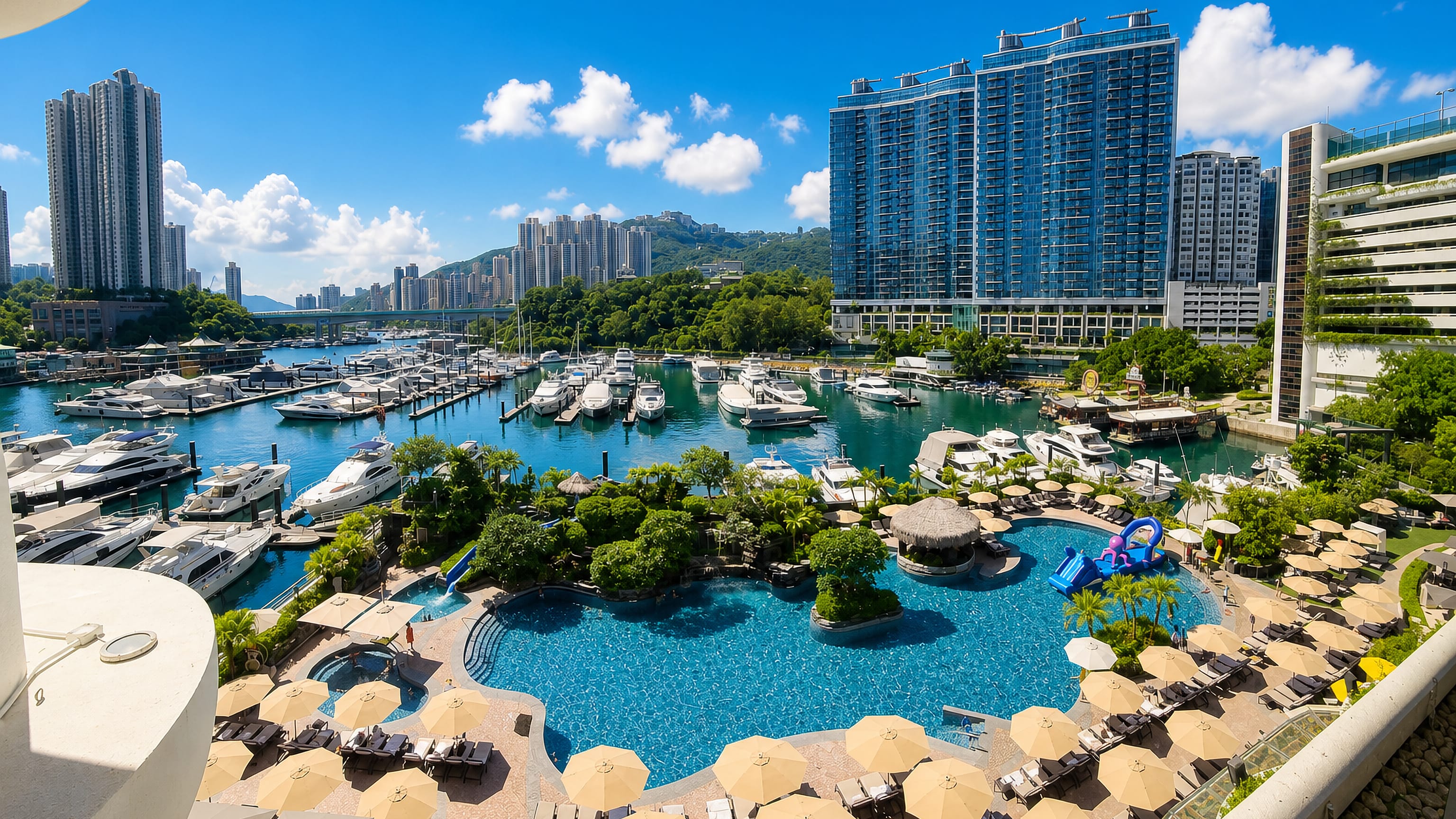 Yacht marina and hillside towers of Aberdeen, Hong Kong, seen over a waterfront hotel pool deck.