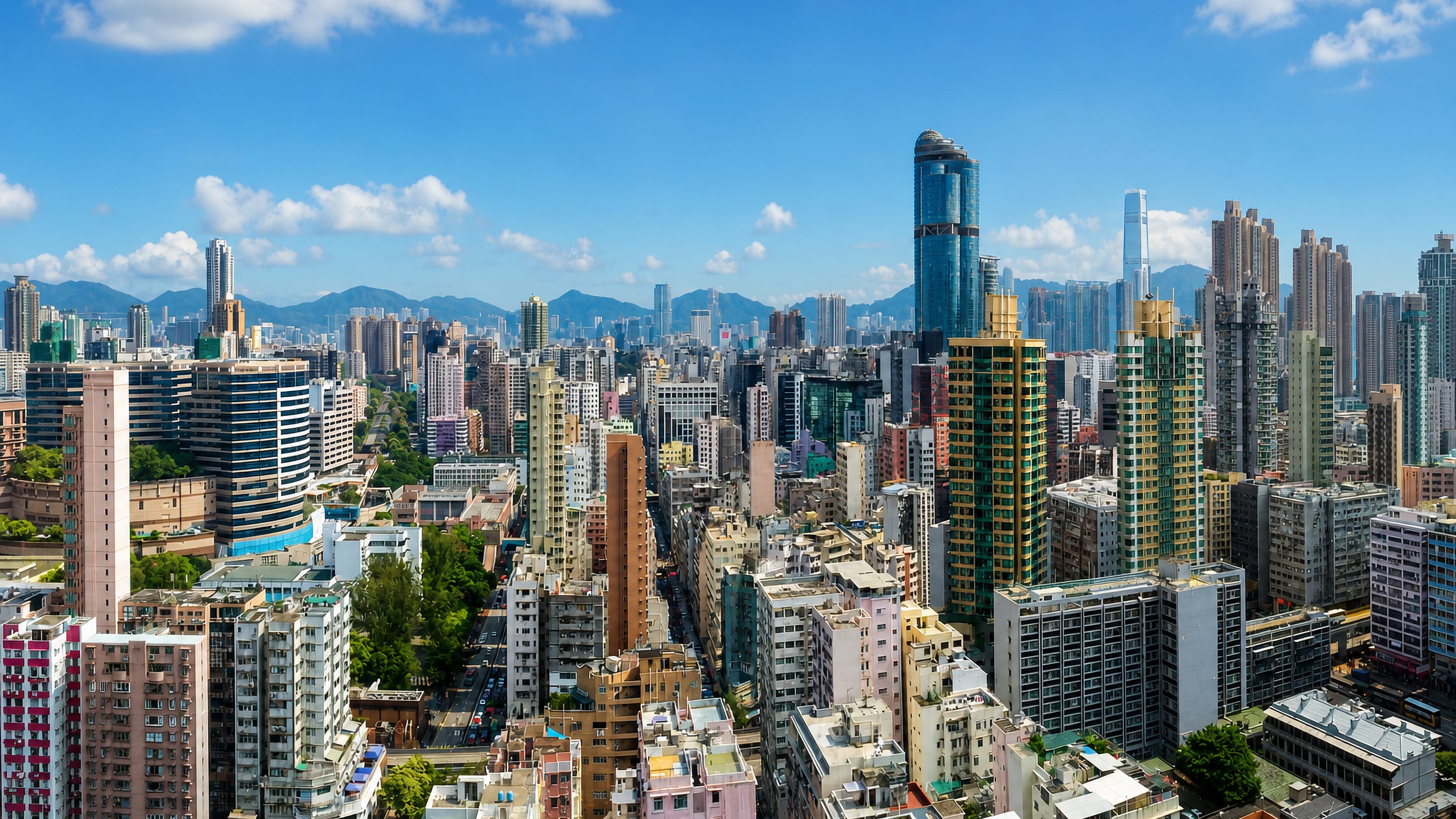 Dense high-rise skyline of Mong Kok, Hong Kong, with a blue glass tower and hills beyond.