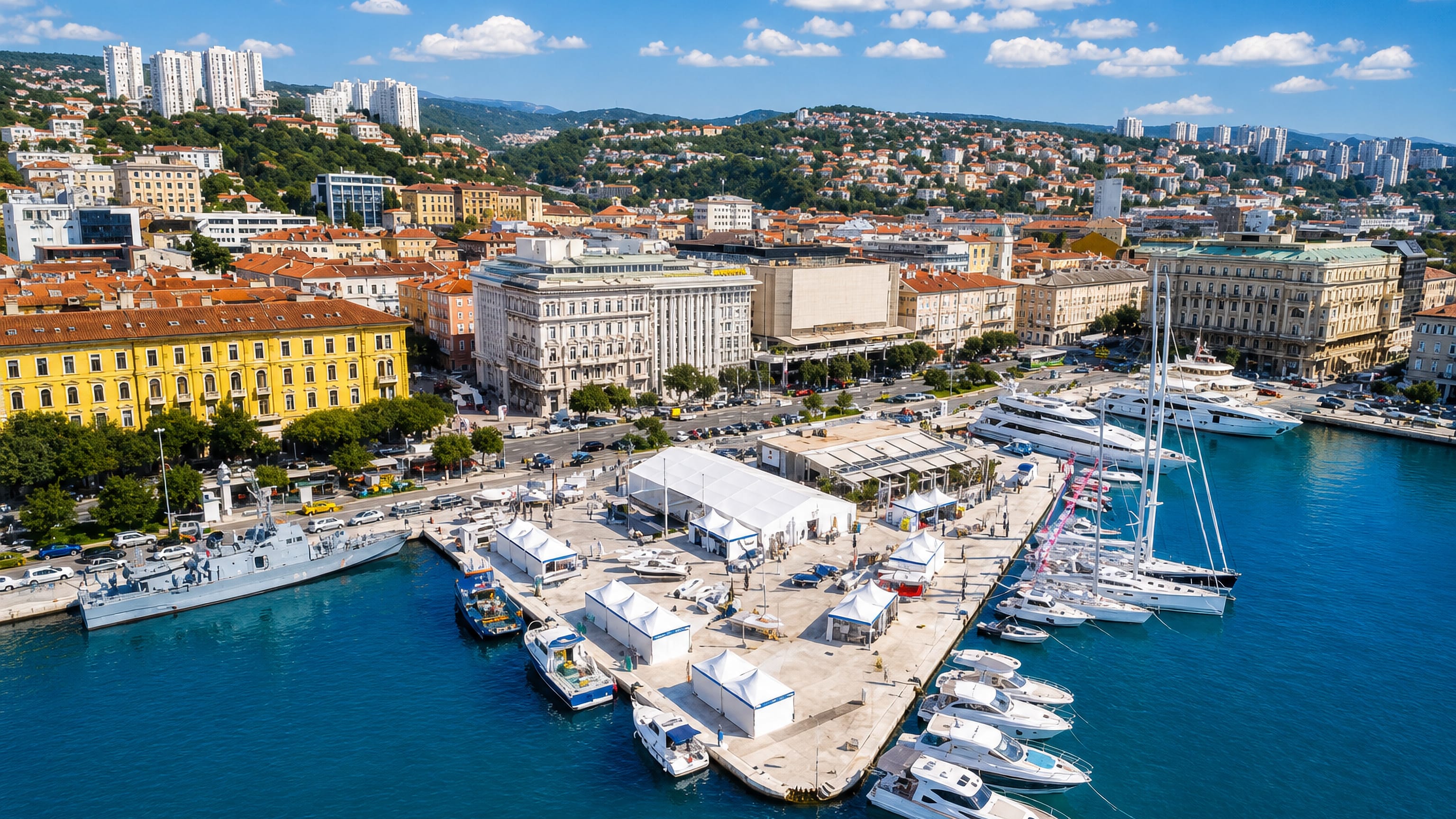 Rijeka's harbour from above, yachts along the pier and the Riva's historic facades below wooded hillsides.