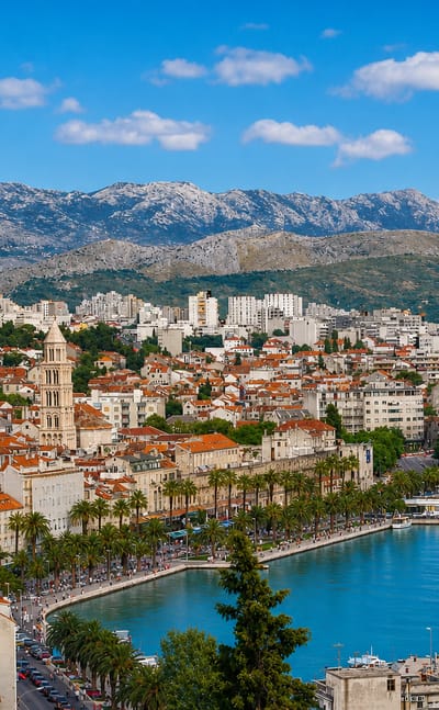 Split's Old Town with the Cathedral of St. Domnius bell tower, red-tiled roofs, palm-lined Riva and harbor below the Mosor mountains.