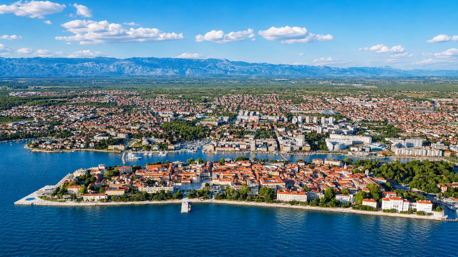Aerial of Zadar's old town peninsula with red roofs, marina and the Adriatic backed by the Velebit mountains, Croatia