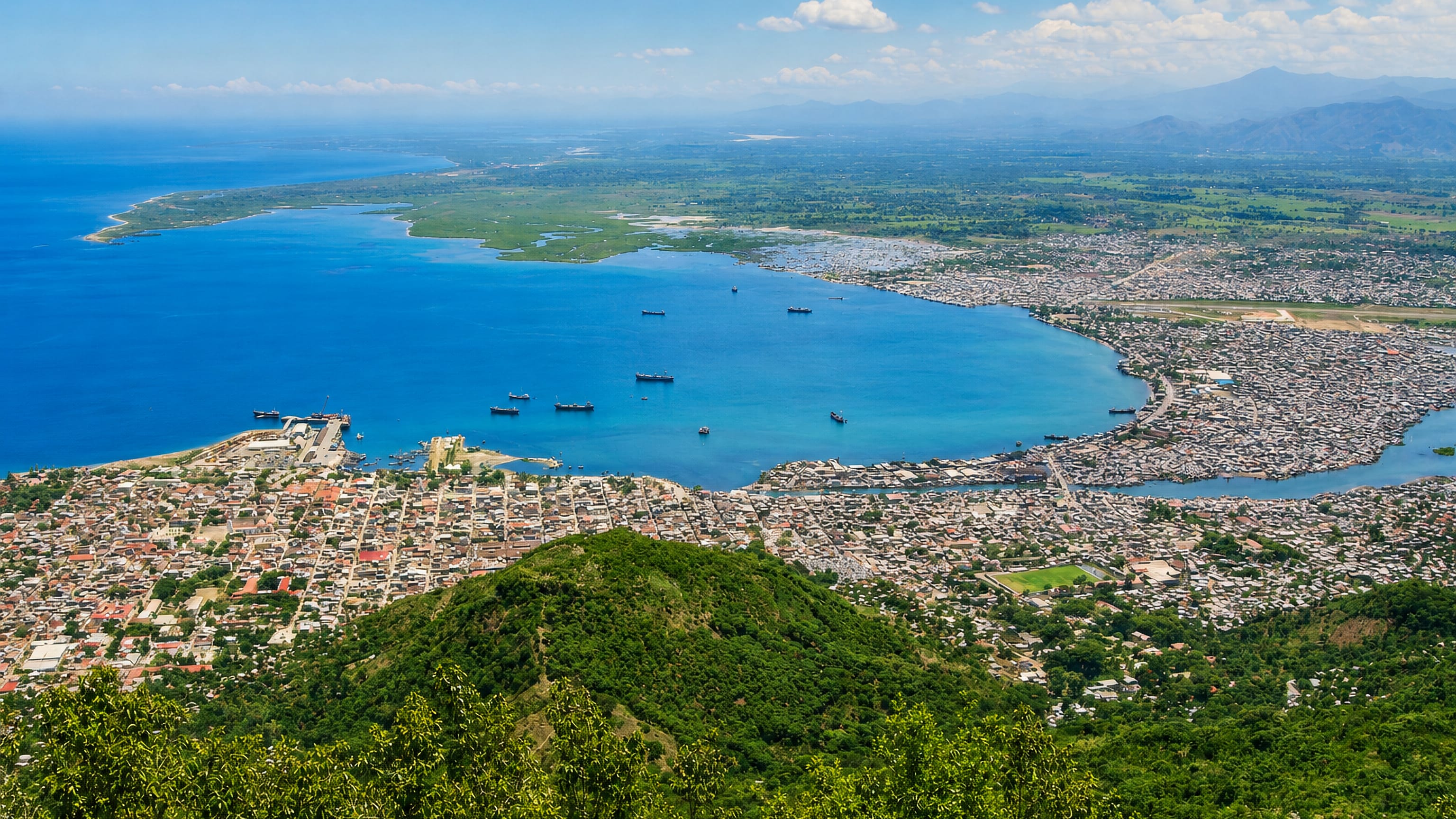 Cap-Haitien and its harbour bay seen from the green hills, with cargo ships anchored offshore in northern Haiti.