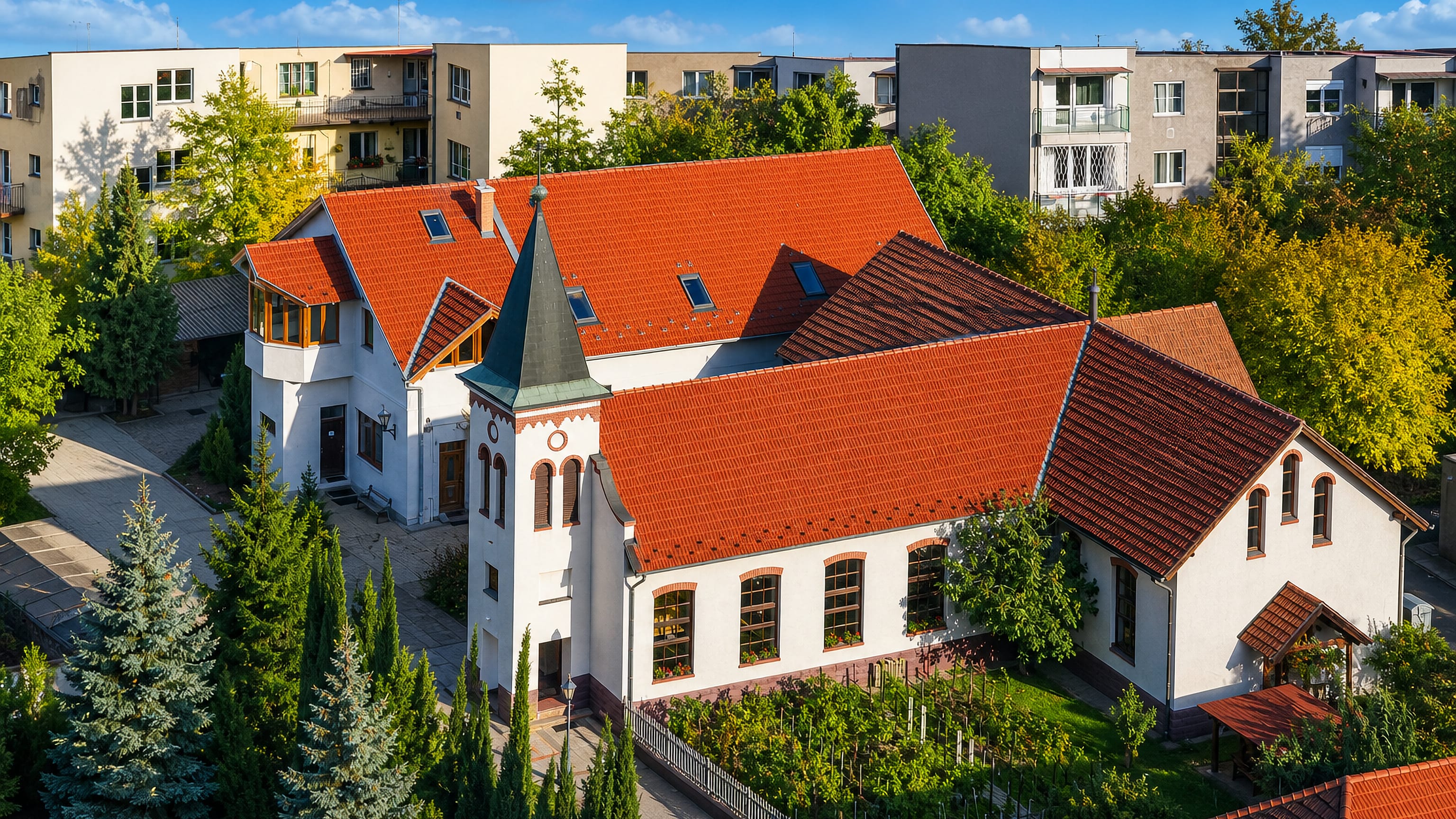 A white church with red tile roof and green spire among panel-block housing in Pesterzsébet, Budapest.